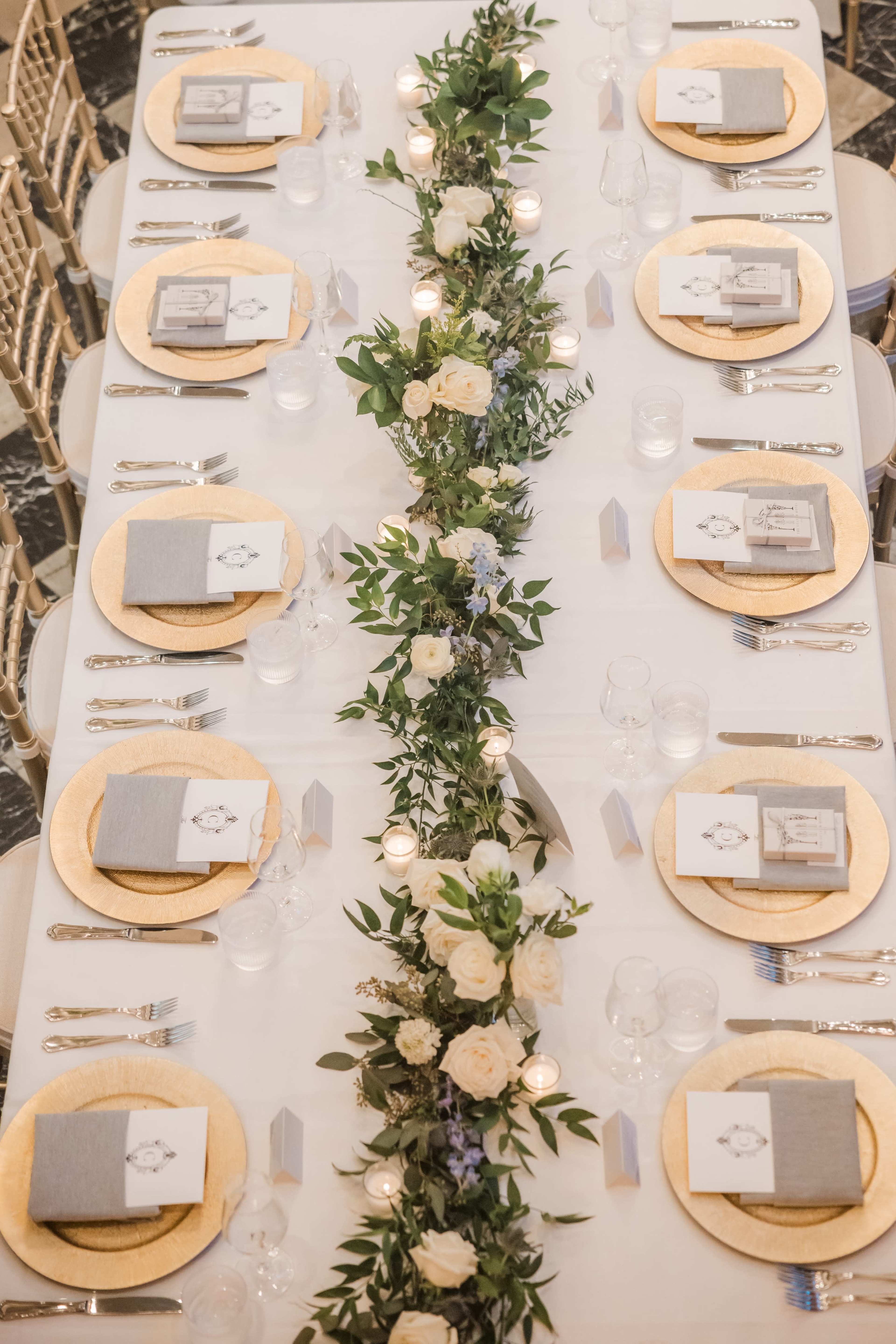 A decorated dining table features gold-rimmed plates, elegant napkins, and a floral centerpiece with candles.