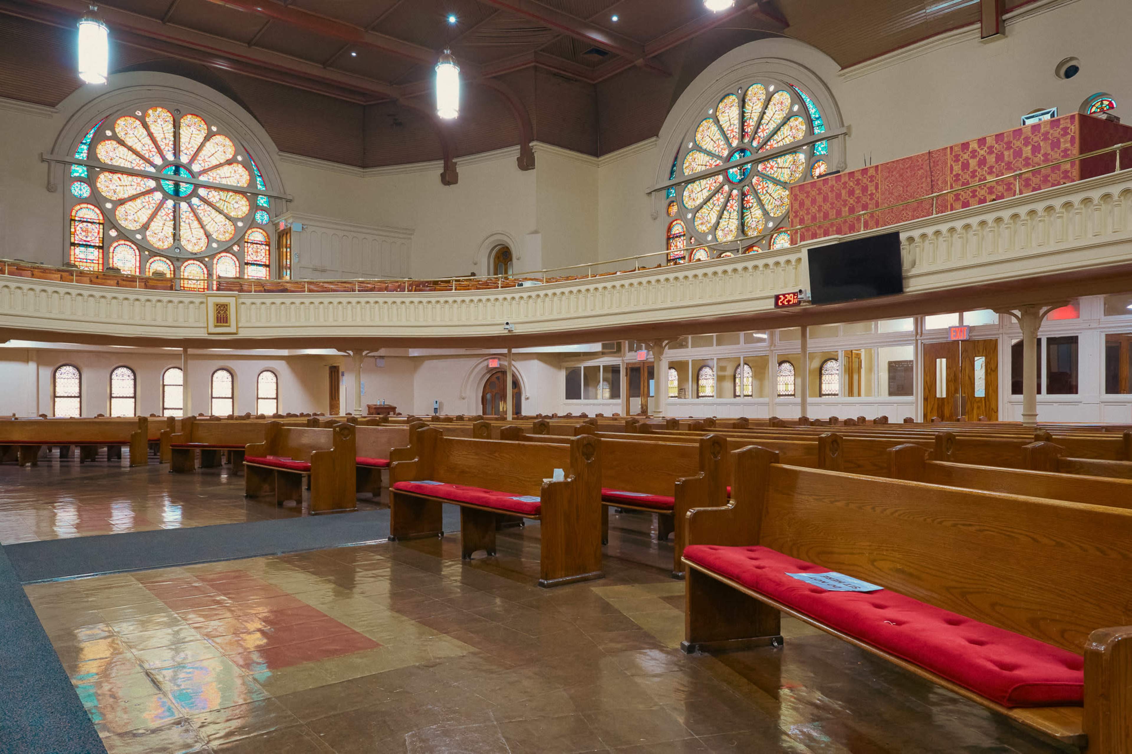 The interior of a spacious church features wooden pews, colorful stained glass windows, and a balcony overlooking the main area.