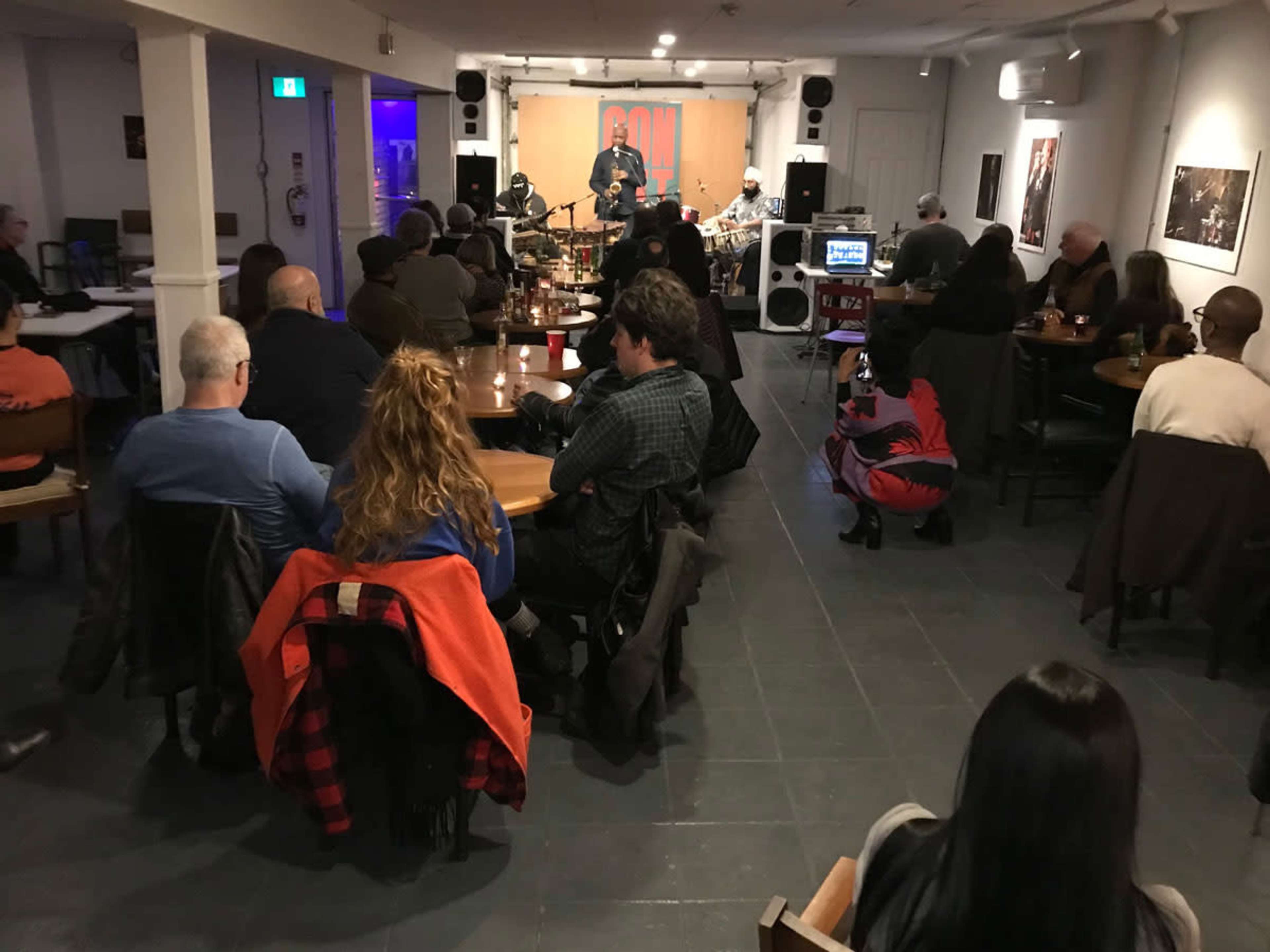 A group of people is seated at tables watching a live musical performance in a small venue.