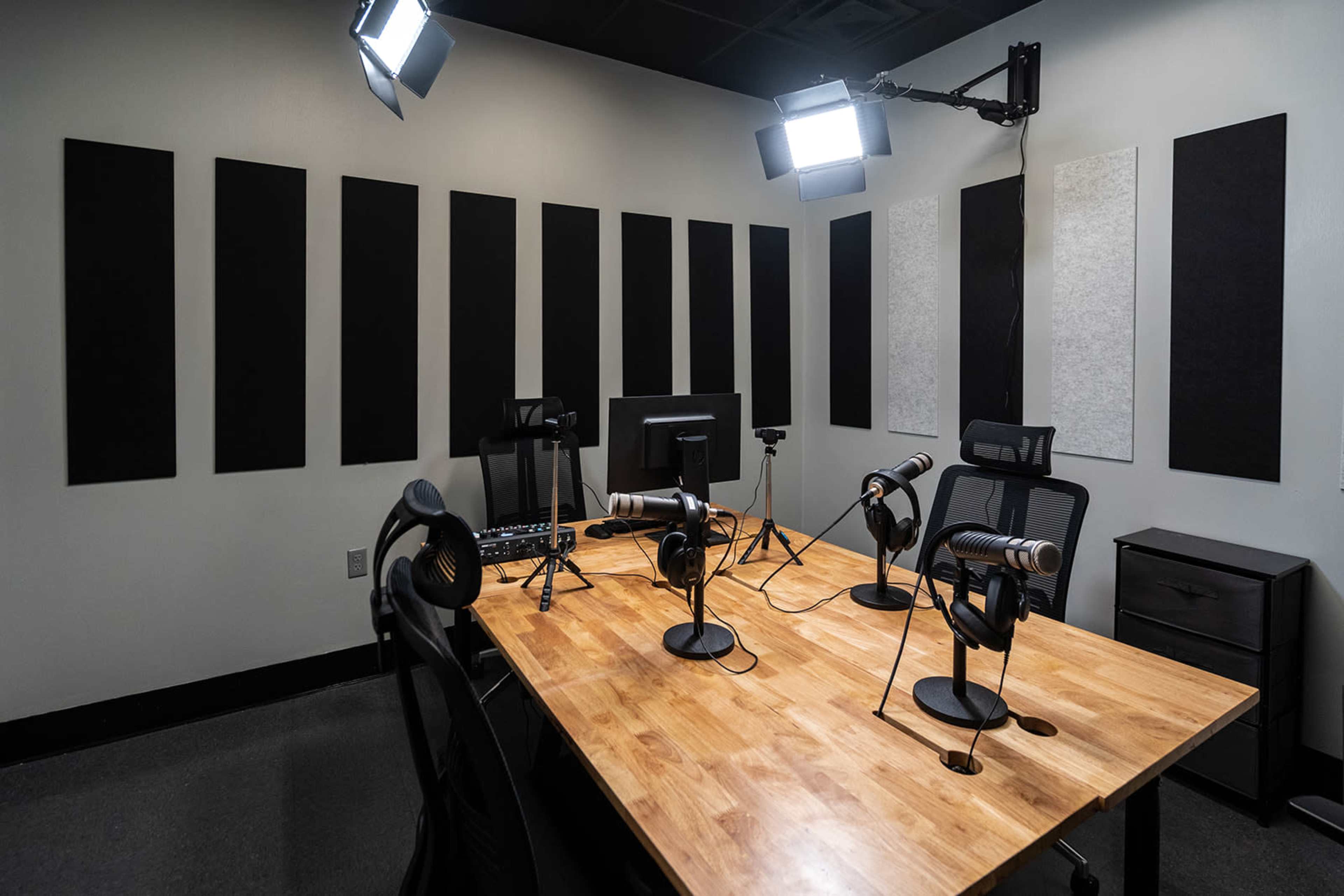 A soundproof recording studio features a wooden table with multiple microphones and headphones, accompanied by sound-absorbing panels on the walls.