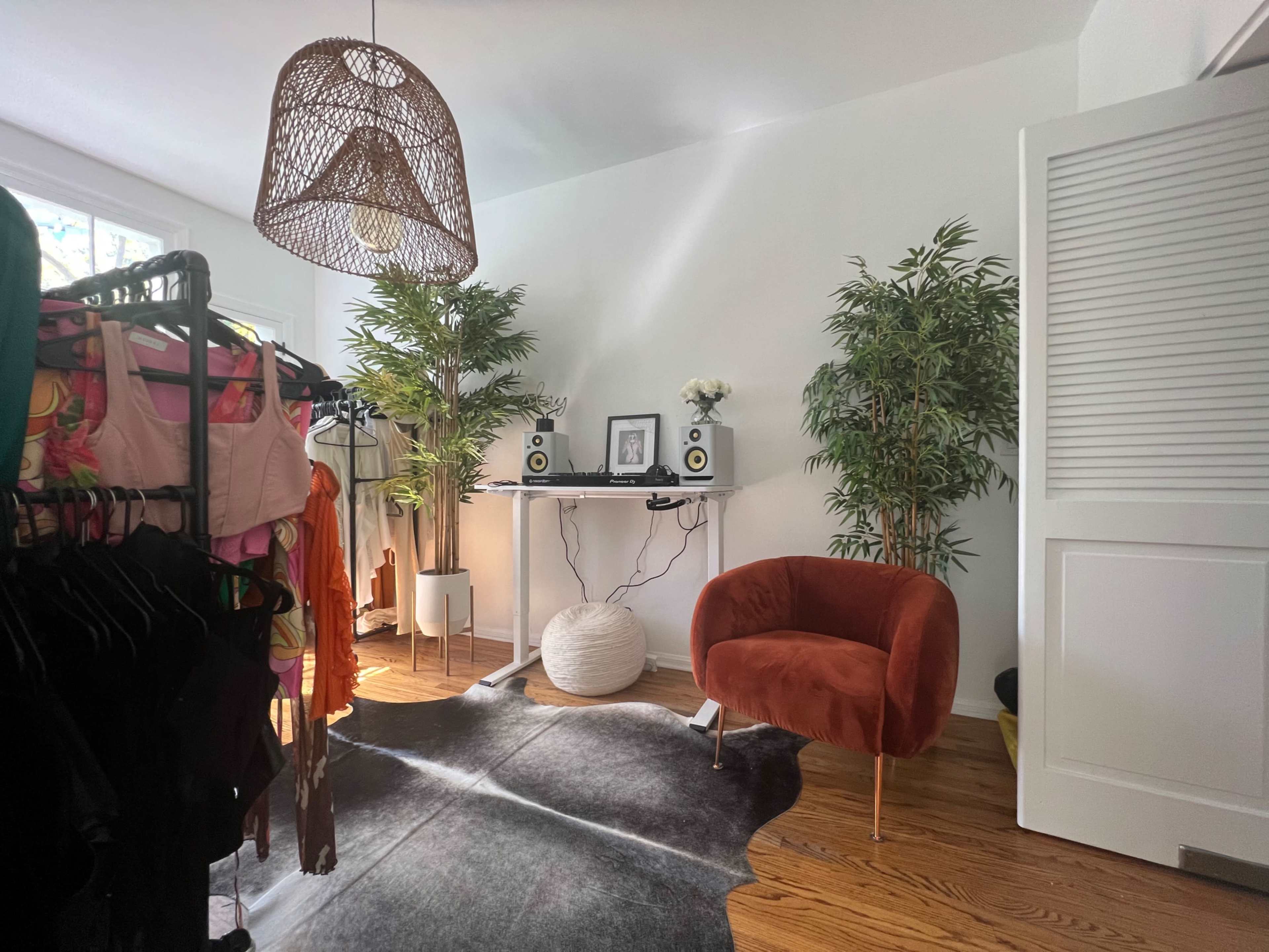 A well-lit room featuring a clothing rack filled with garments, a pair of speakers on a table, a potted plant, and a cozy orange chair.