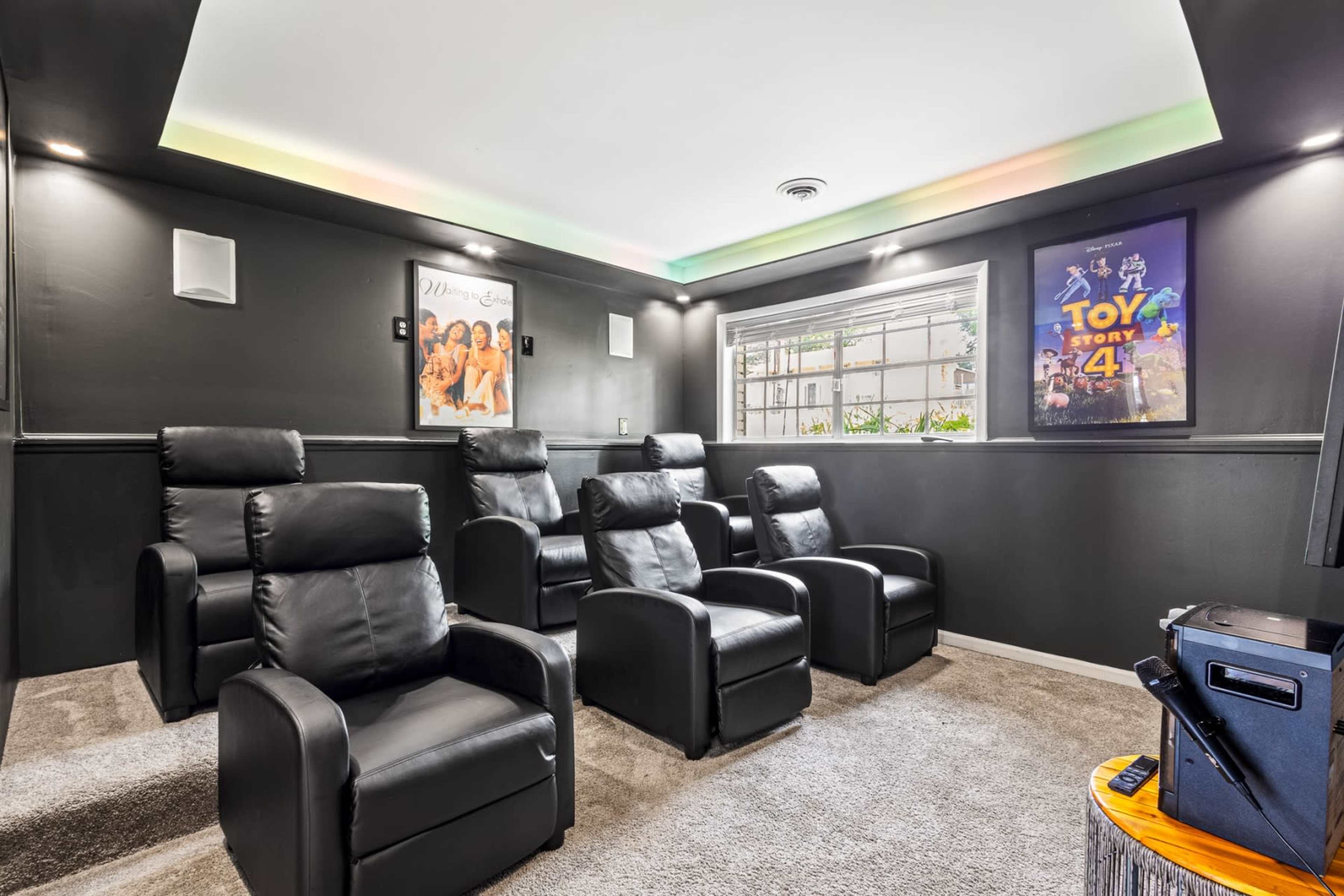 The image shows a home theater with four leather reclining chairs, a movie poster on the wall, and ambient lighting around the ceiling.