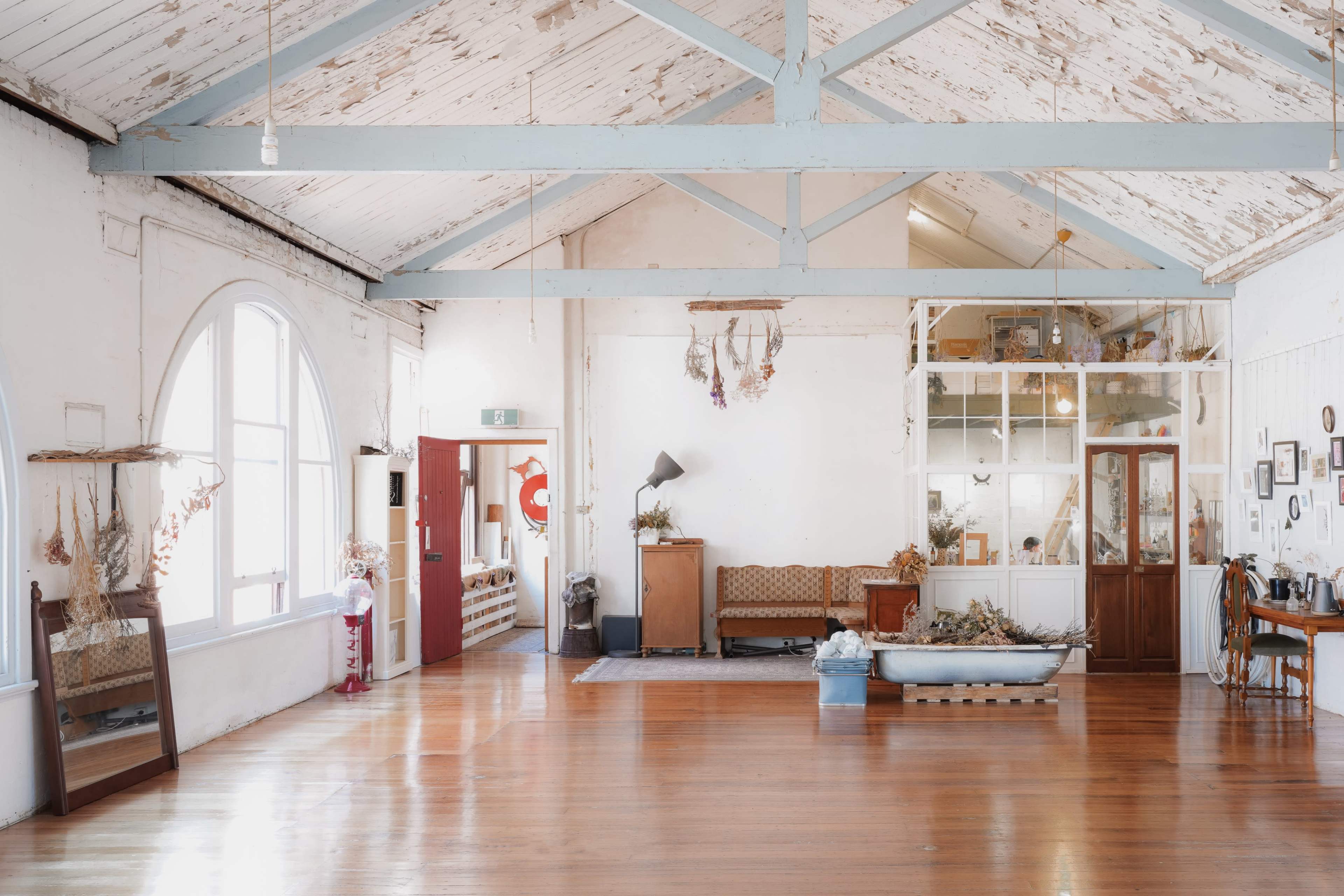 The image shows a spacious, well-lit room with high ceilings, wooden floors, and various decorative items, including a sofa and a display cabinet.