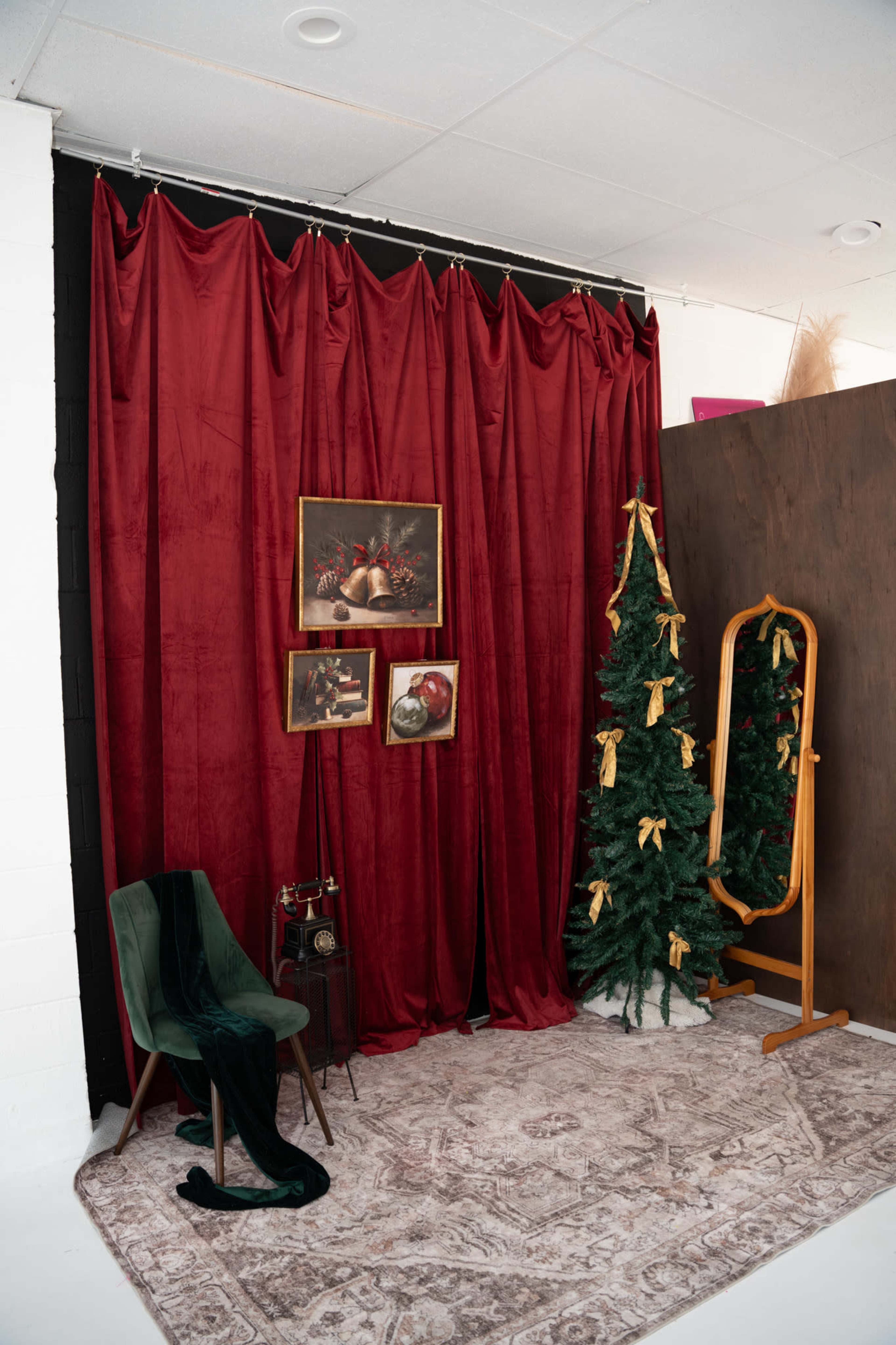 The scene features a cozy corner with a rich red curtain, two decorated Christmas trees, a mirror, an antique chair, and framed artwork on the wall.