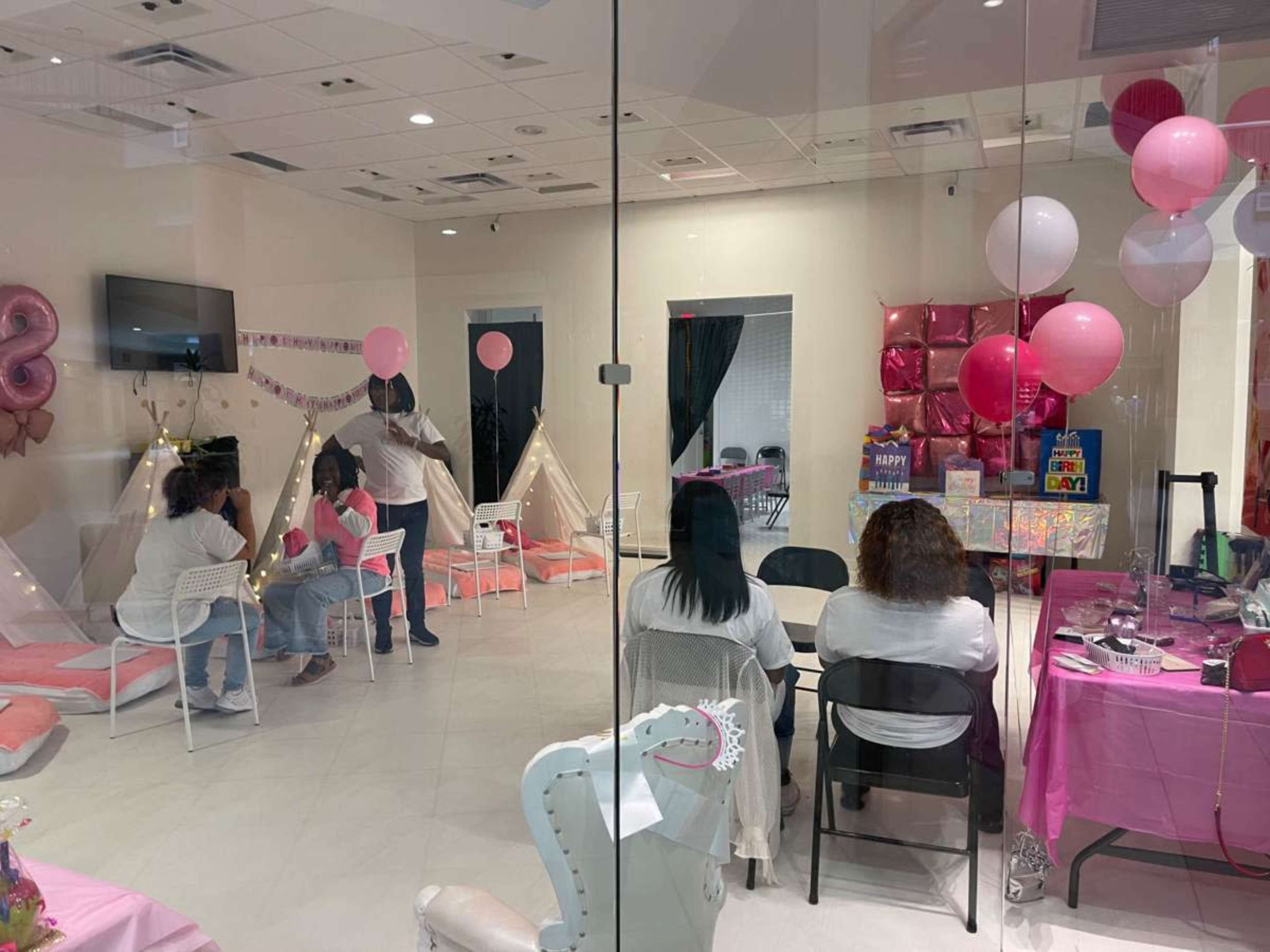 The image shows a children's party venue decorated with pink accents, featuring seating, balloons, and a small play area with tents.