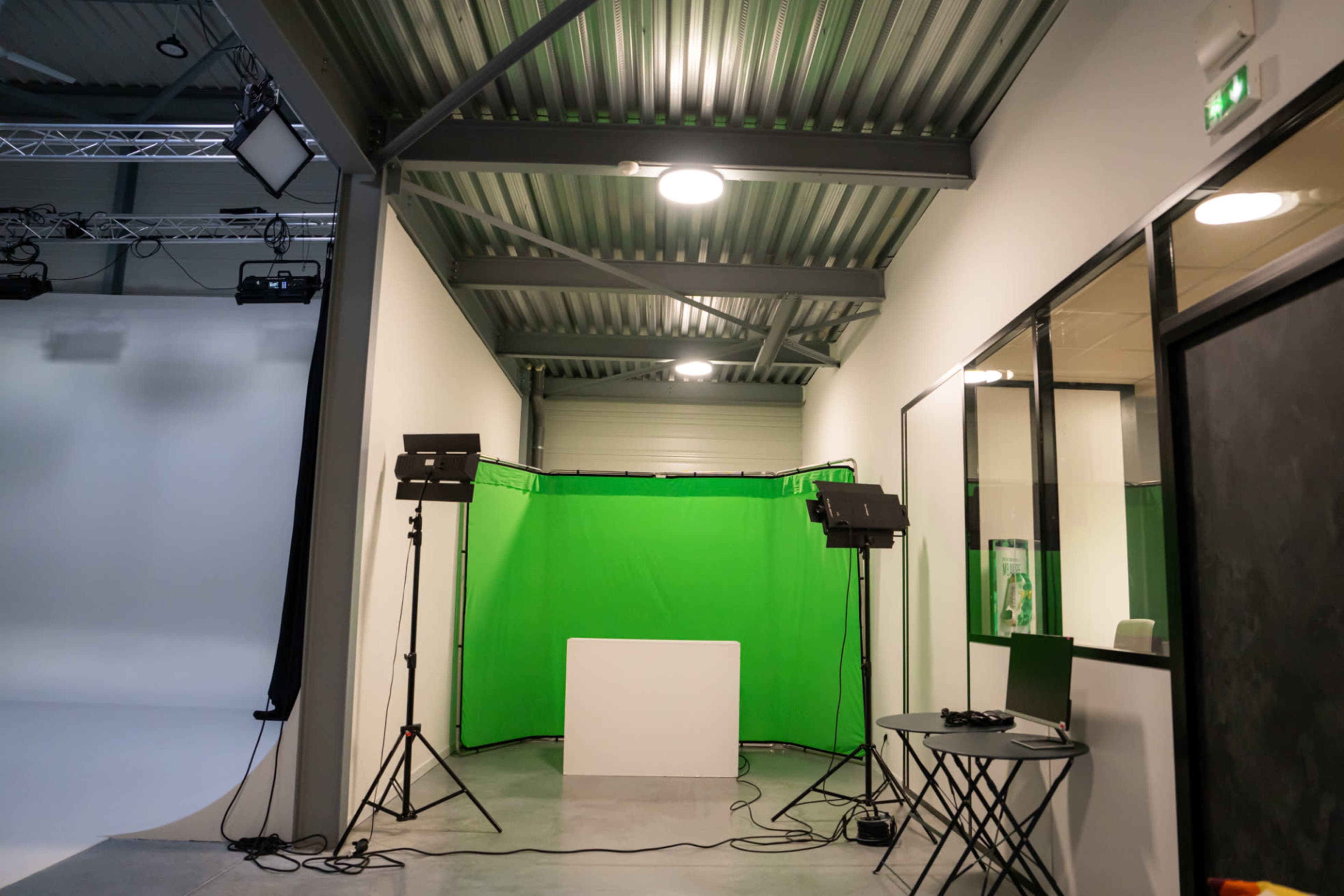 A studio space featuring a green screen backdrop, lighting equipment, and a small table with chairs.