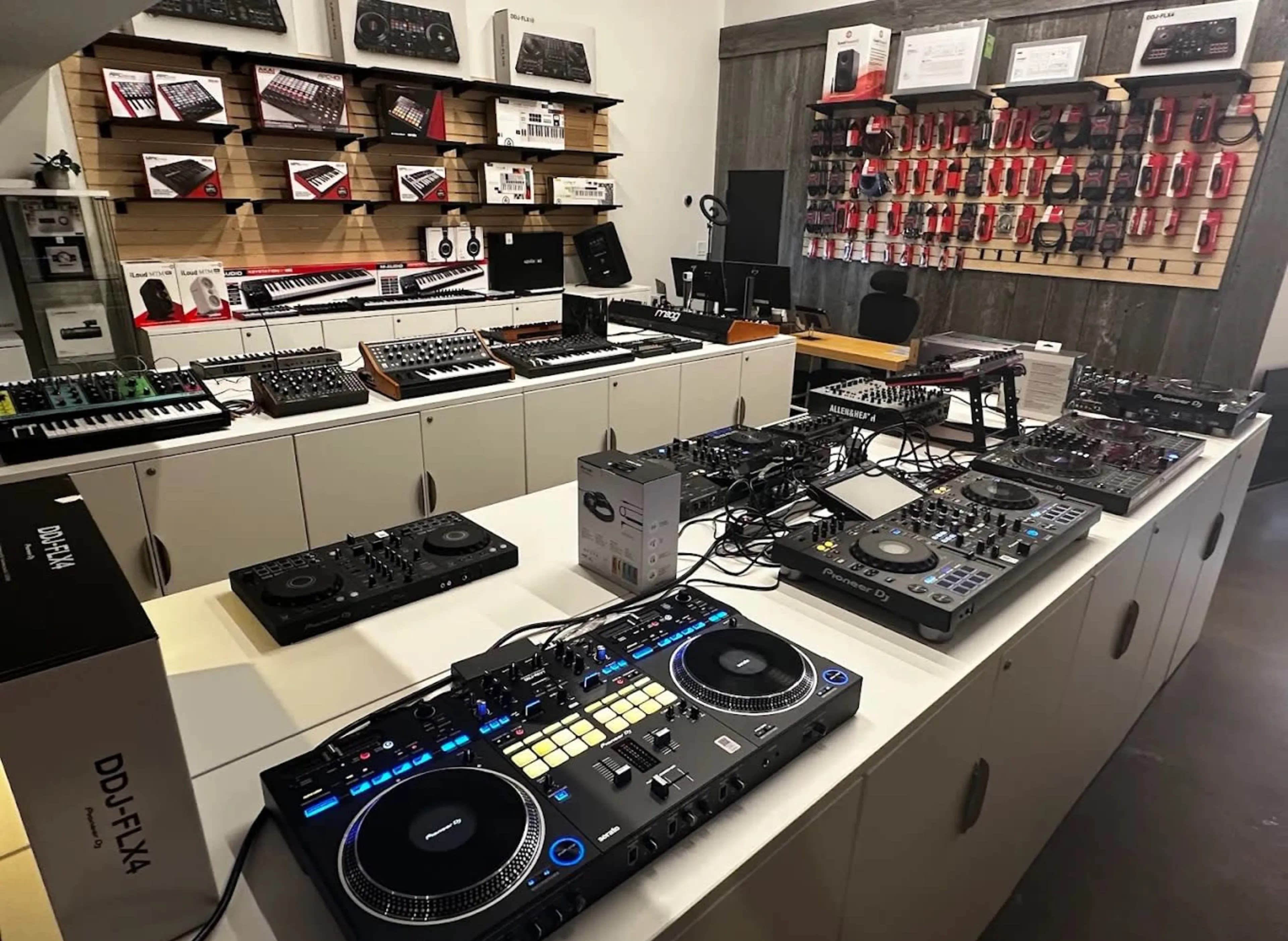 The image shows a music equipment store displaying various DJ gear, synthesizers, and audio devices on shelves and tables.