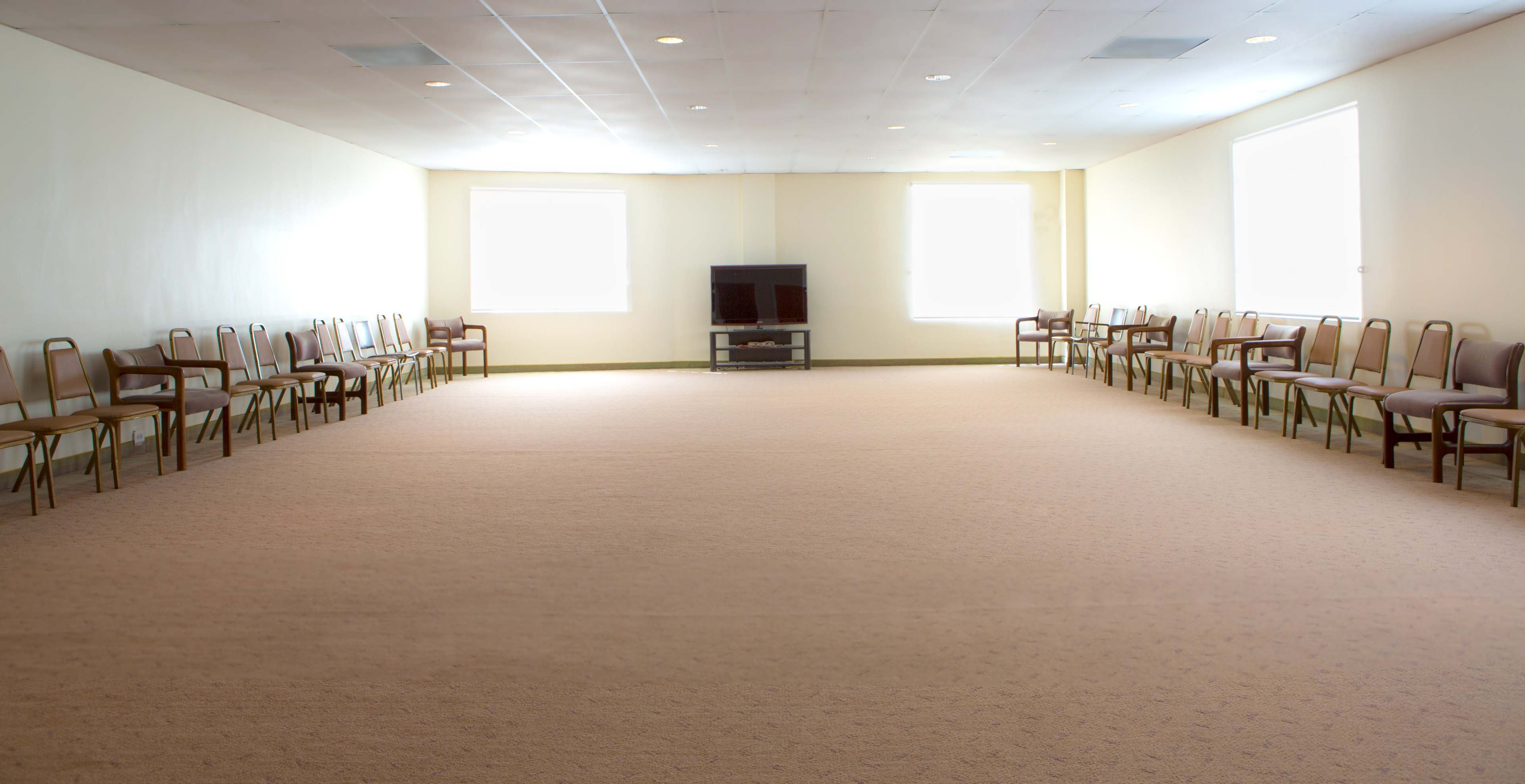 A spacious, empty room with two rows of chairs along the walls and a television set at the far end.