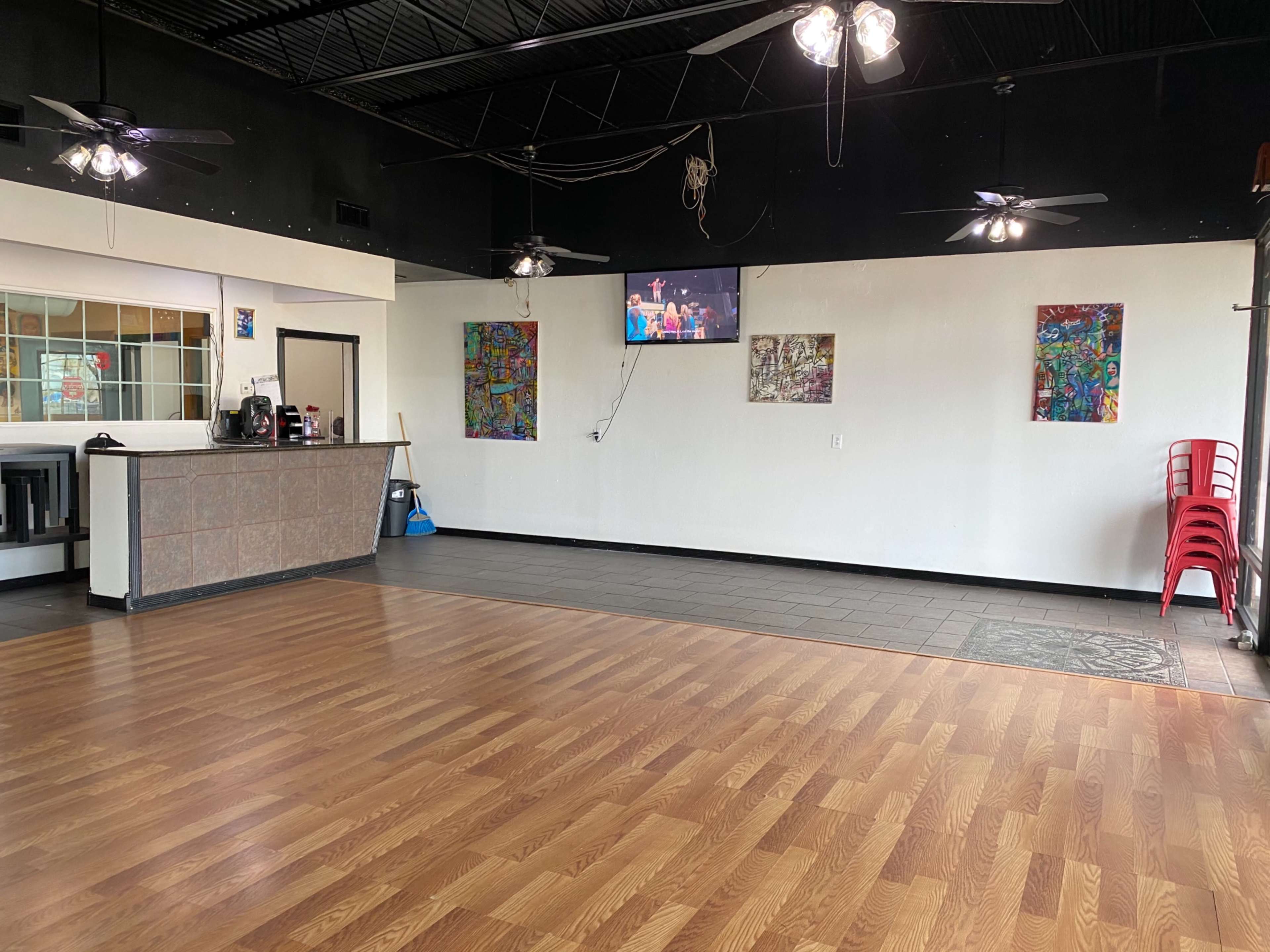 The image shows an empty dining area with a service counter, colorful artwork on the walls, and a television mounted above.