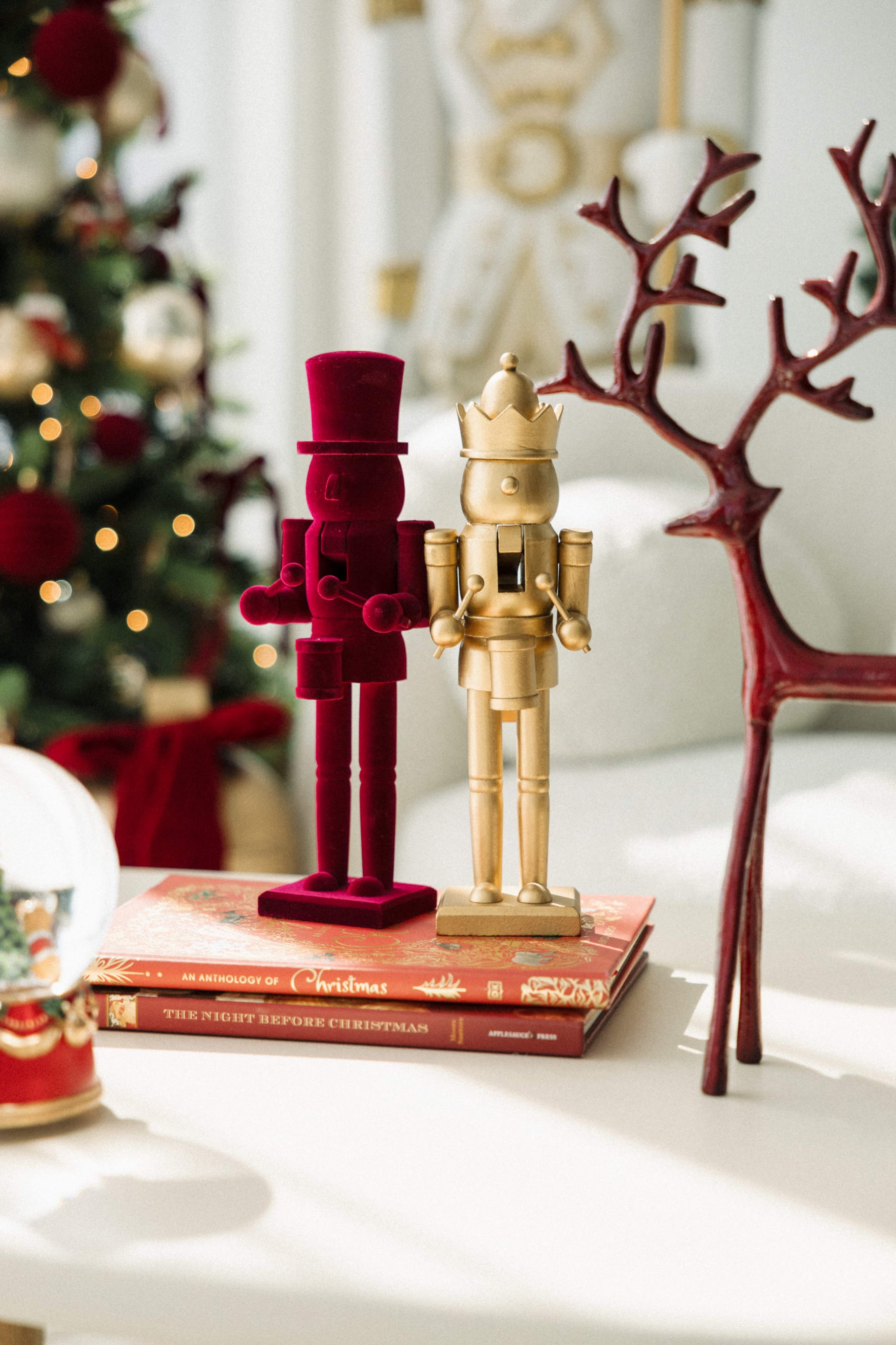 The image features red and gold nutcracker figurines standing on a stack of Christmas-themed books, with a decorated tree and a reindeer figurine in the background.