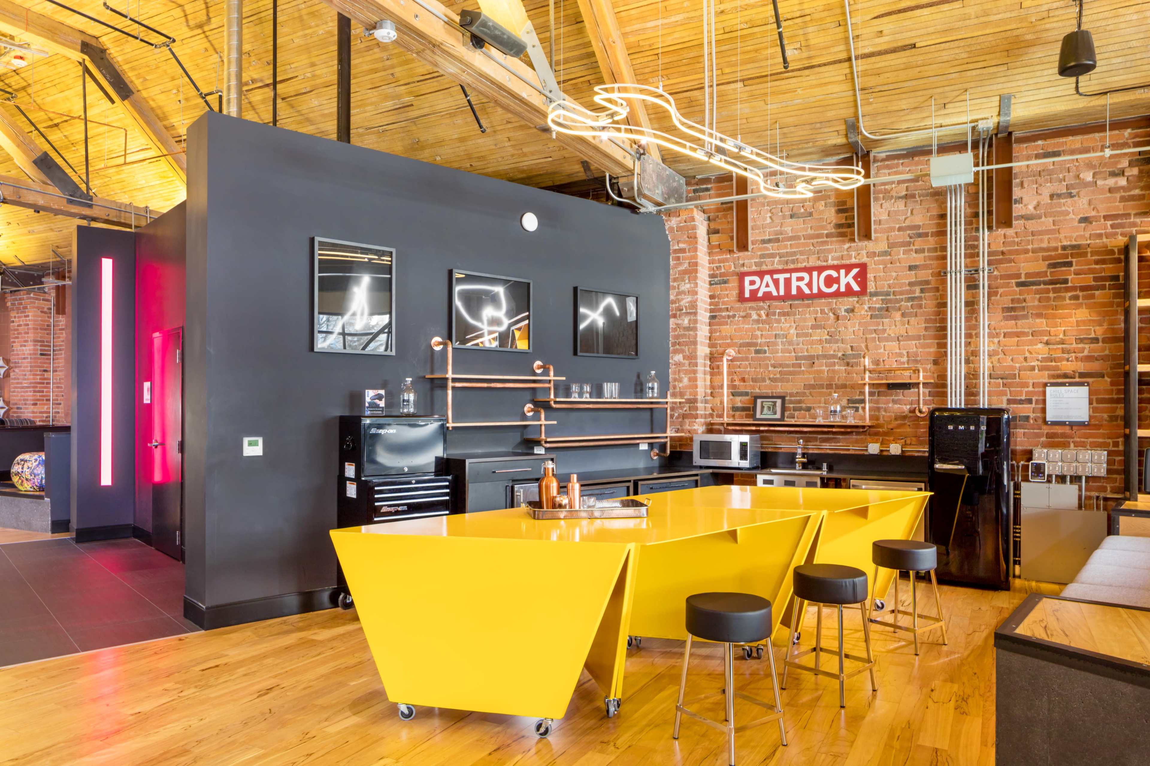 A modern kitchen with a bright yellow island, black cabinetry, and exposed brick walls.