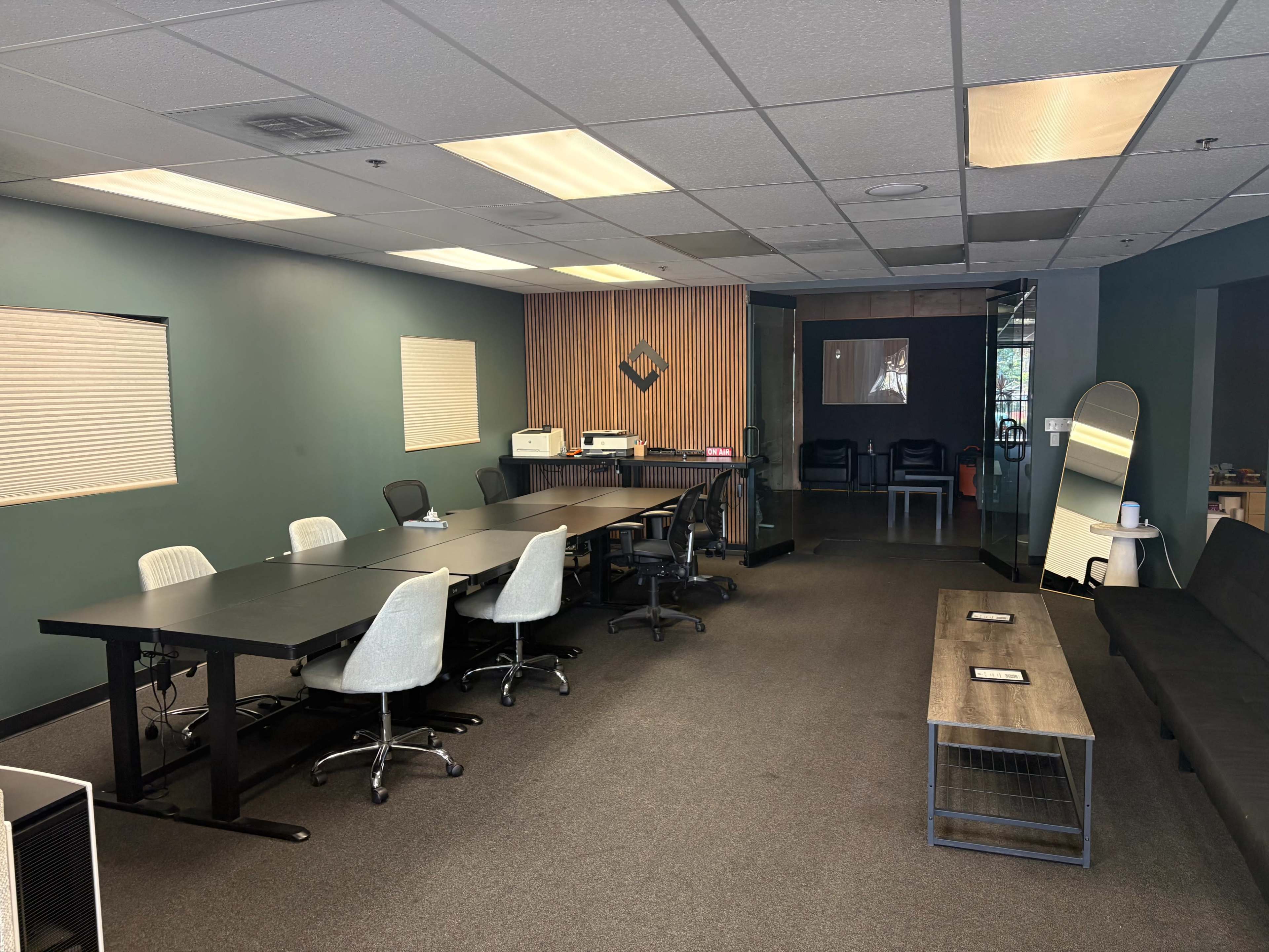 The image shows a modern conference room with a large table and chairs, a printer, and an adjacent seating area.