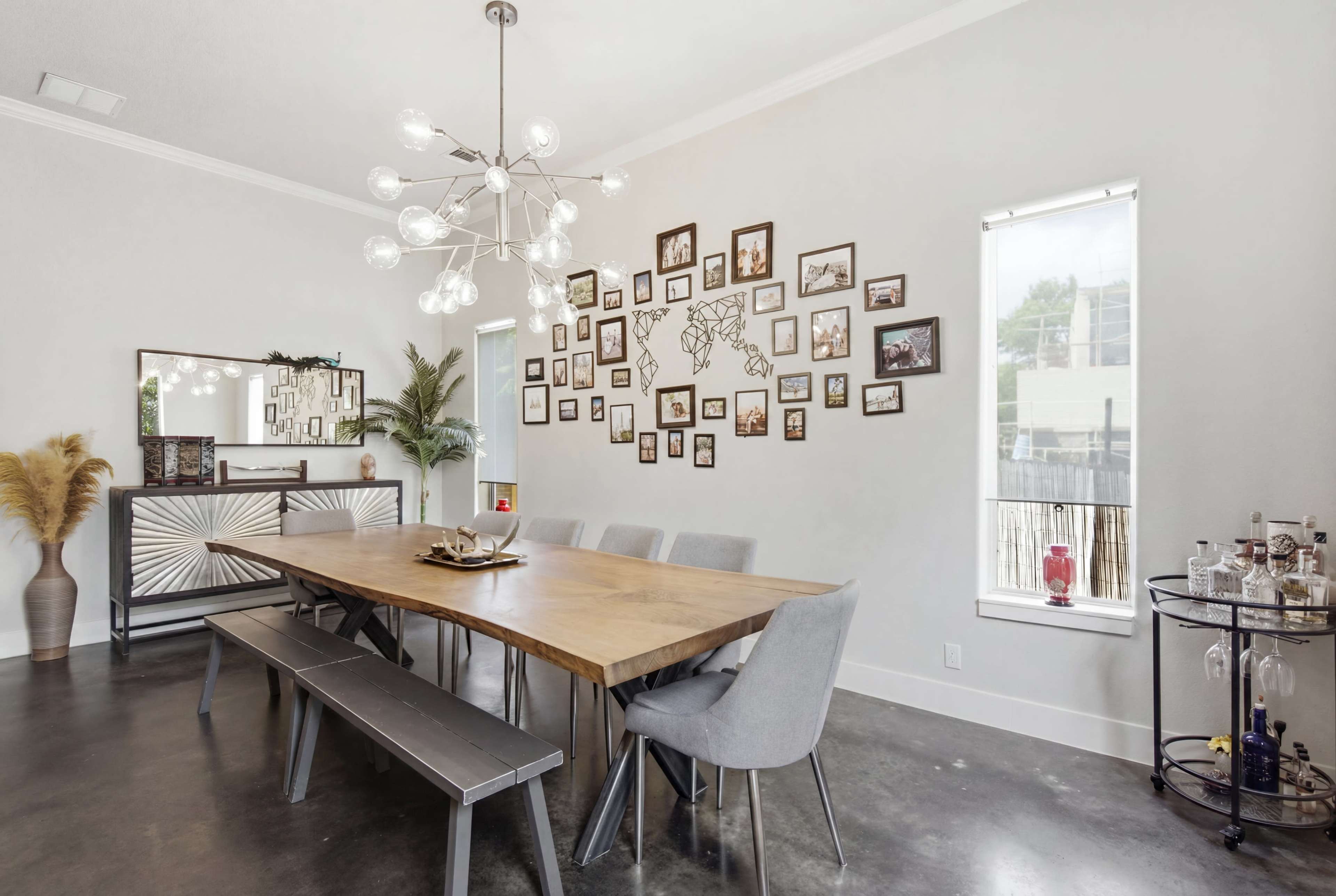 A modern dining area features a wooden table with gray chairs, a decorative wall of framed photos, and a stylish light fixture hanging from the ceiling.
