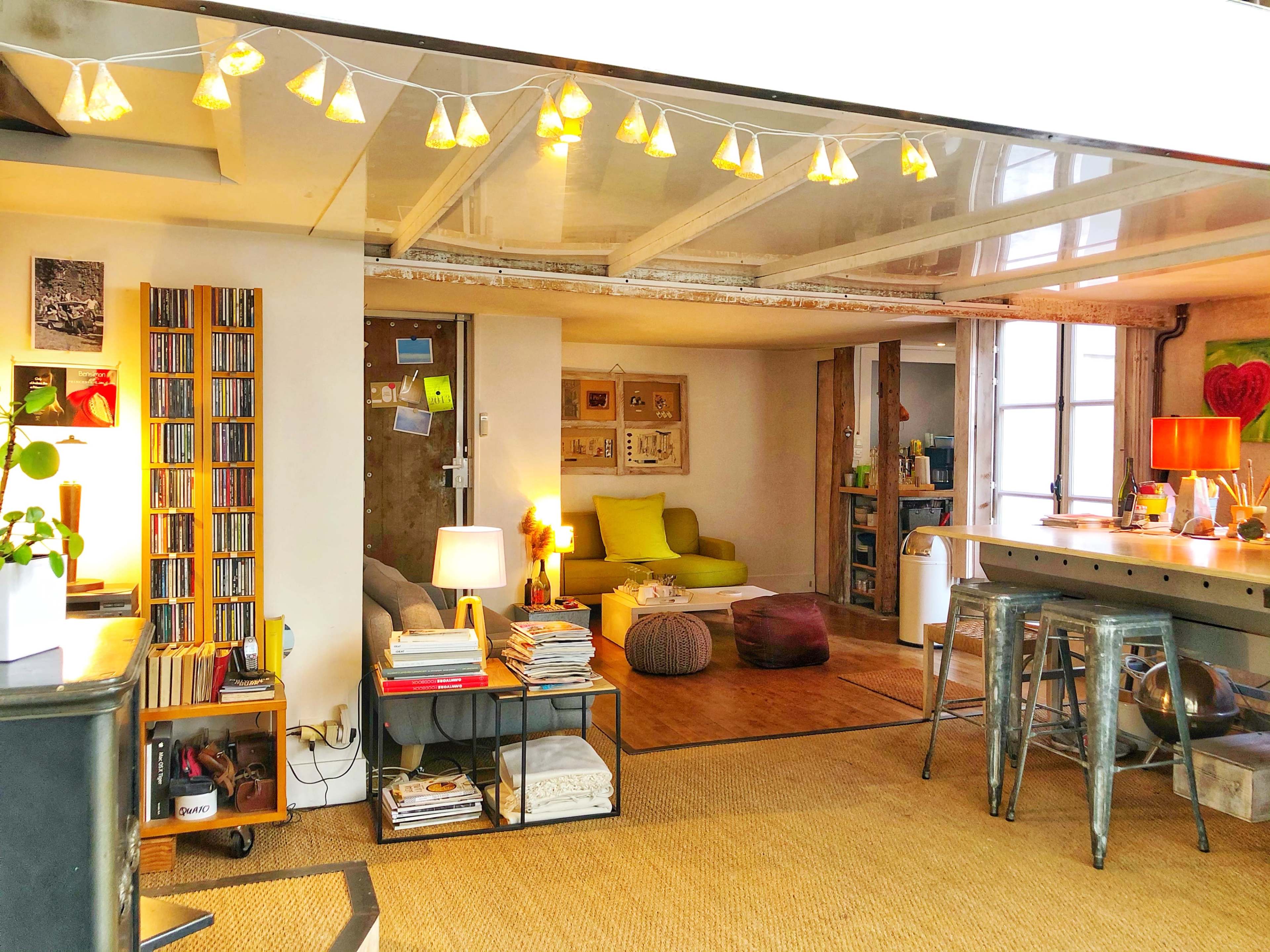 The image shows a cozy open-concept living space with a kitchen area, a seating area featuring a green couch, and shelves filled with books and magazines.