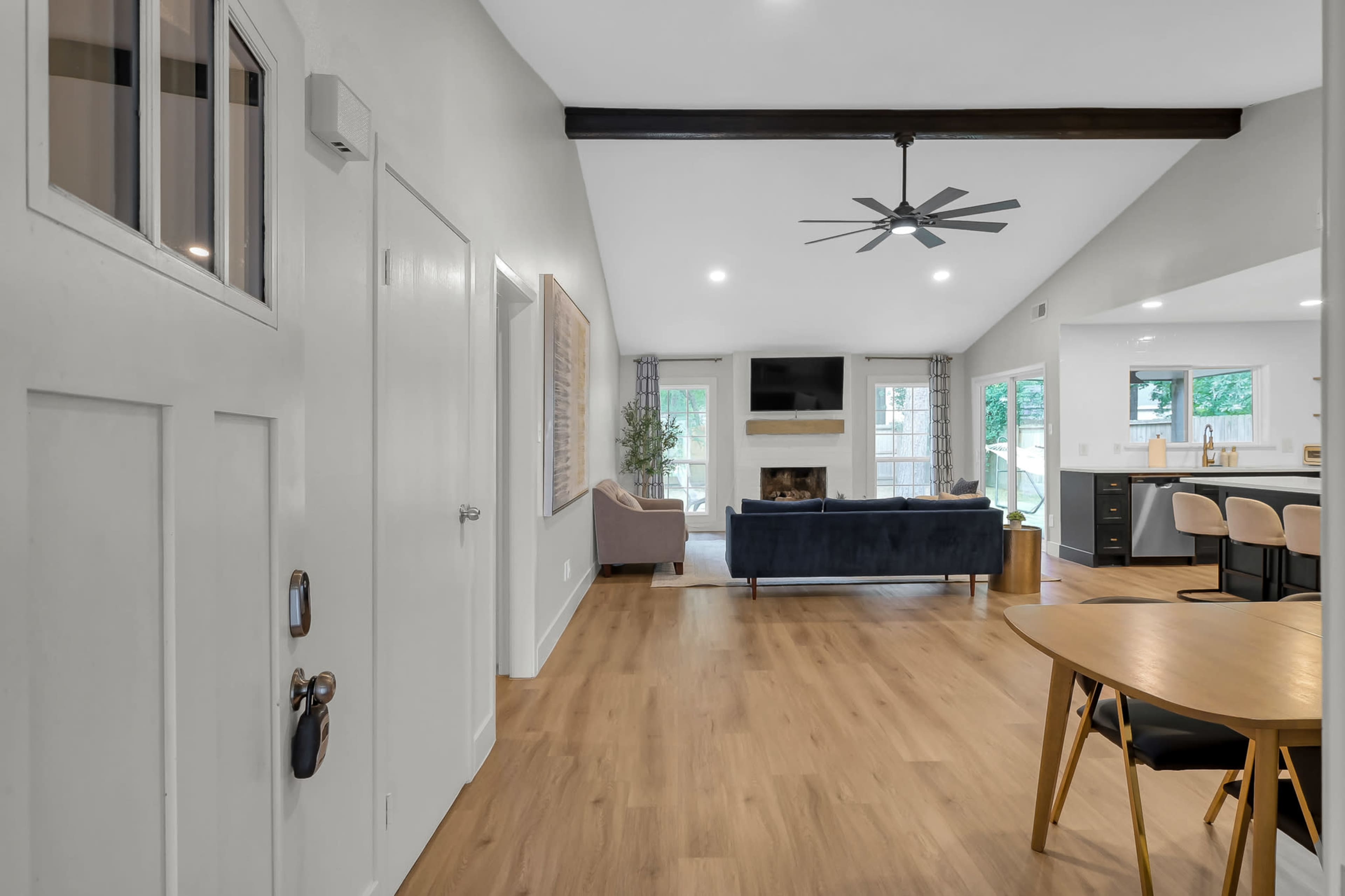 The image shows an open-concept living space featuring a dining area with a round table, a sofa in the lounge area, and large windows providing natural light.