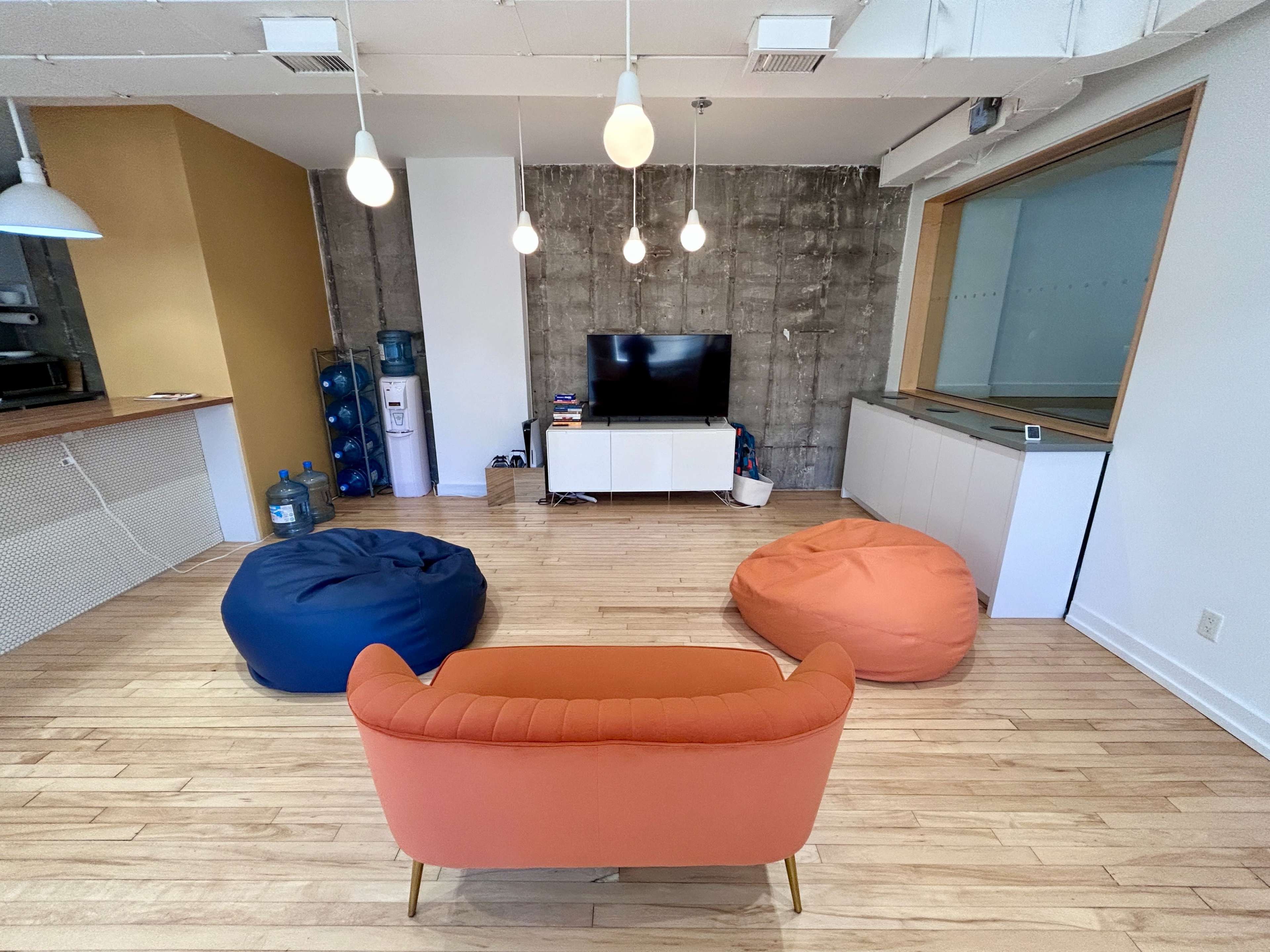 The image shows a modern living space featuring a television on a white media console with two colorful bean bag chairs and a coral couch arranged around it.
