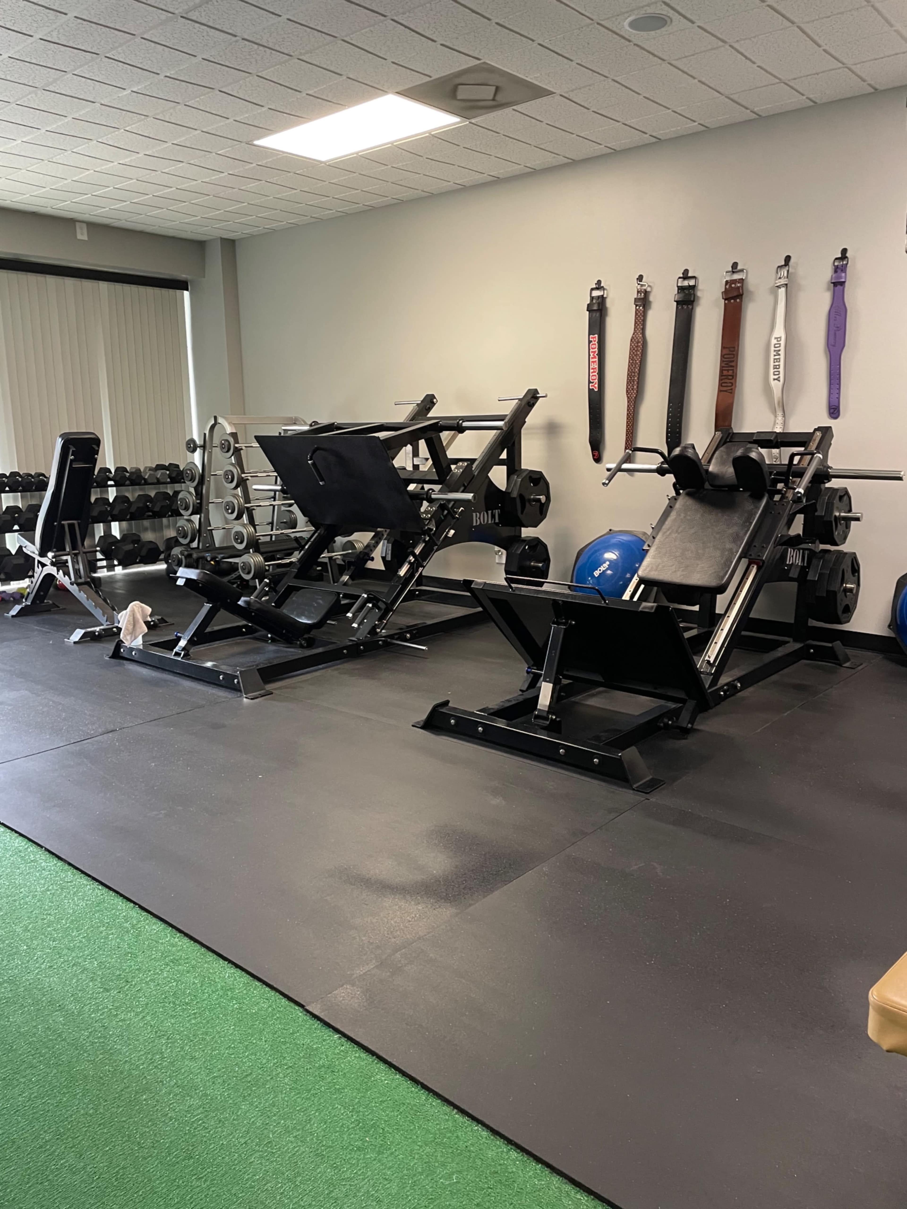 A gym interior with various weightlifting machines, free weights, and exercise equipment arranged on a rubber floor.