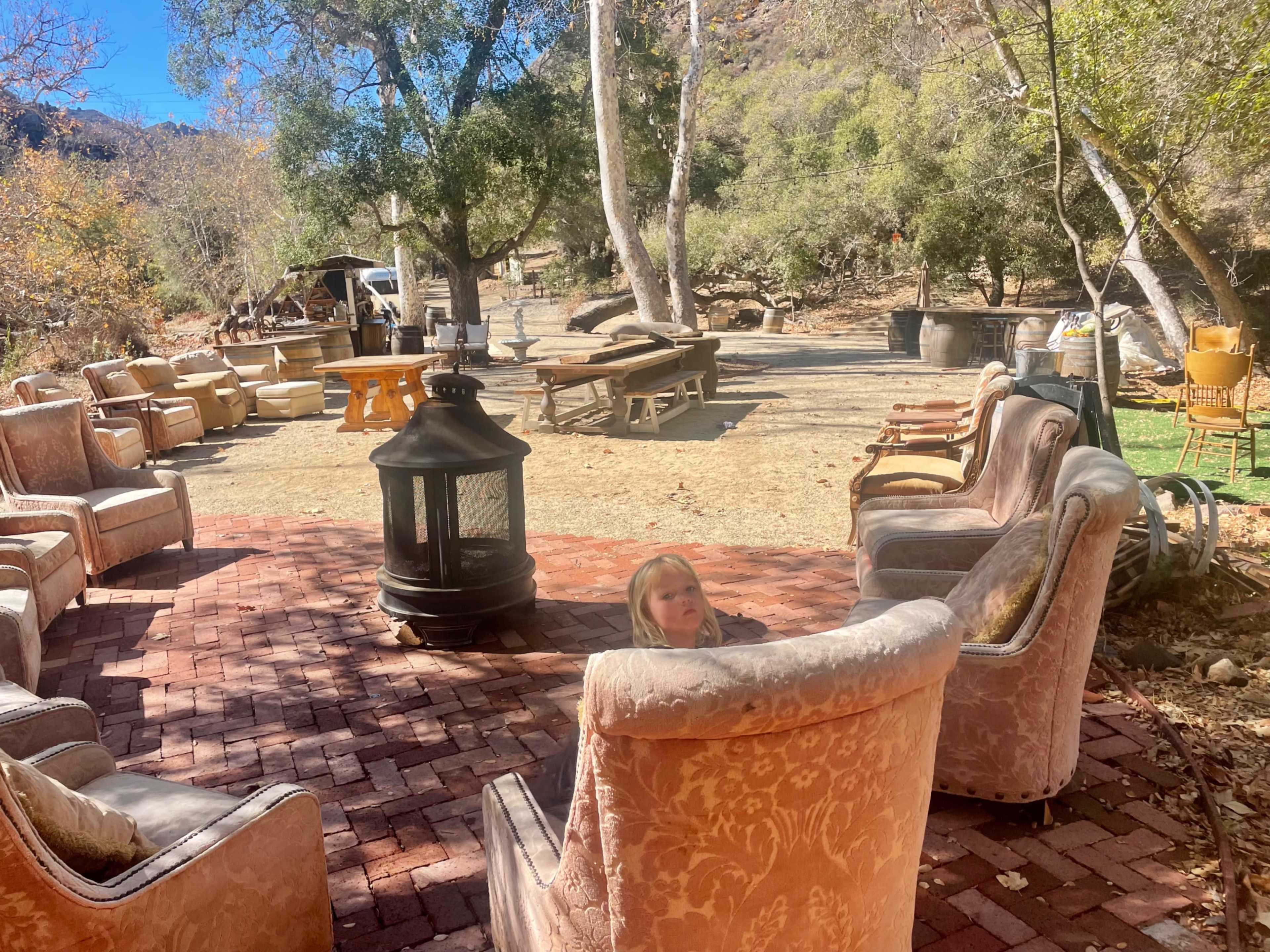 A circle of vintage chairs surrounds a decorative lantern in an outdoor setting with scattered tables and greenery.