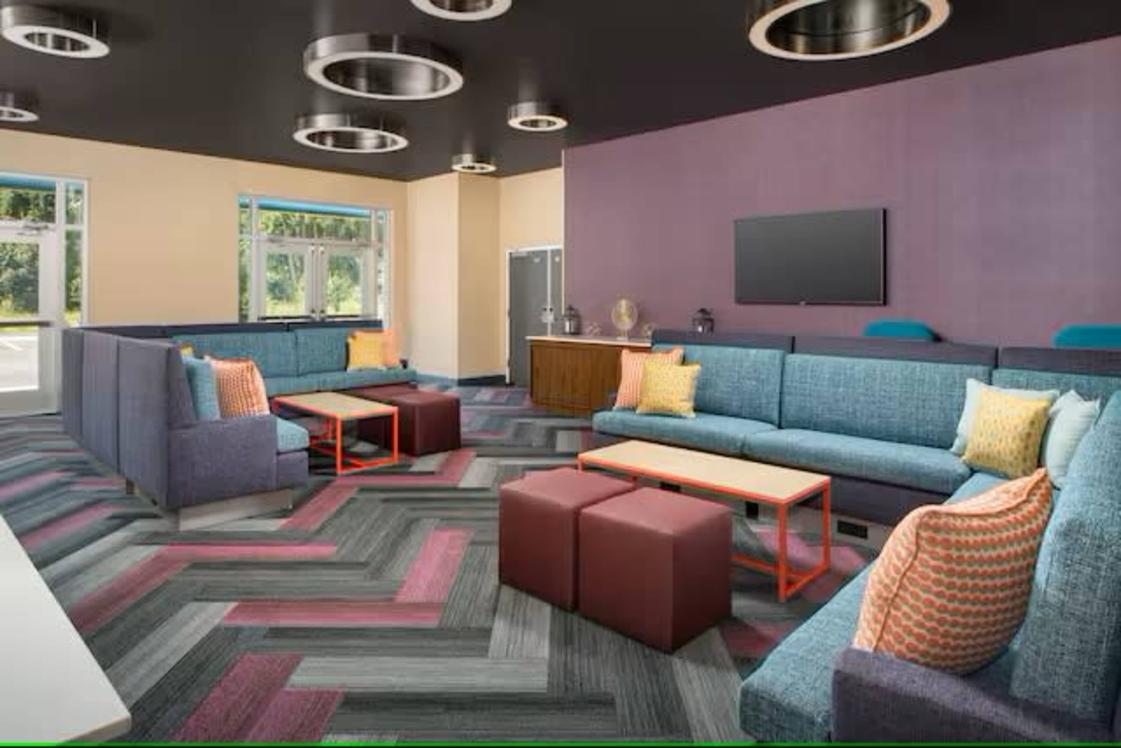 The image shows a modern lounge area with colorful seating, a central coffee table, and a large wall-mounted television.