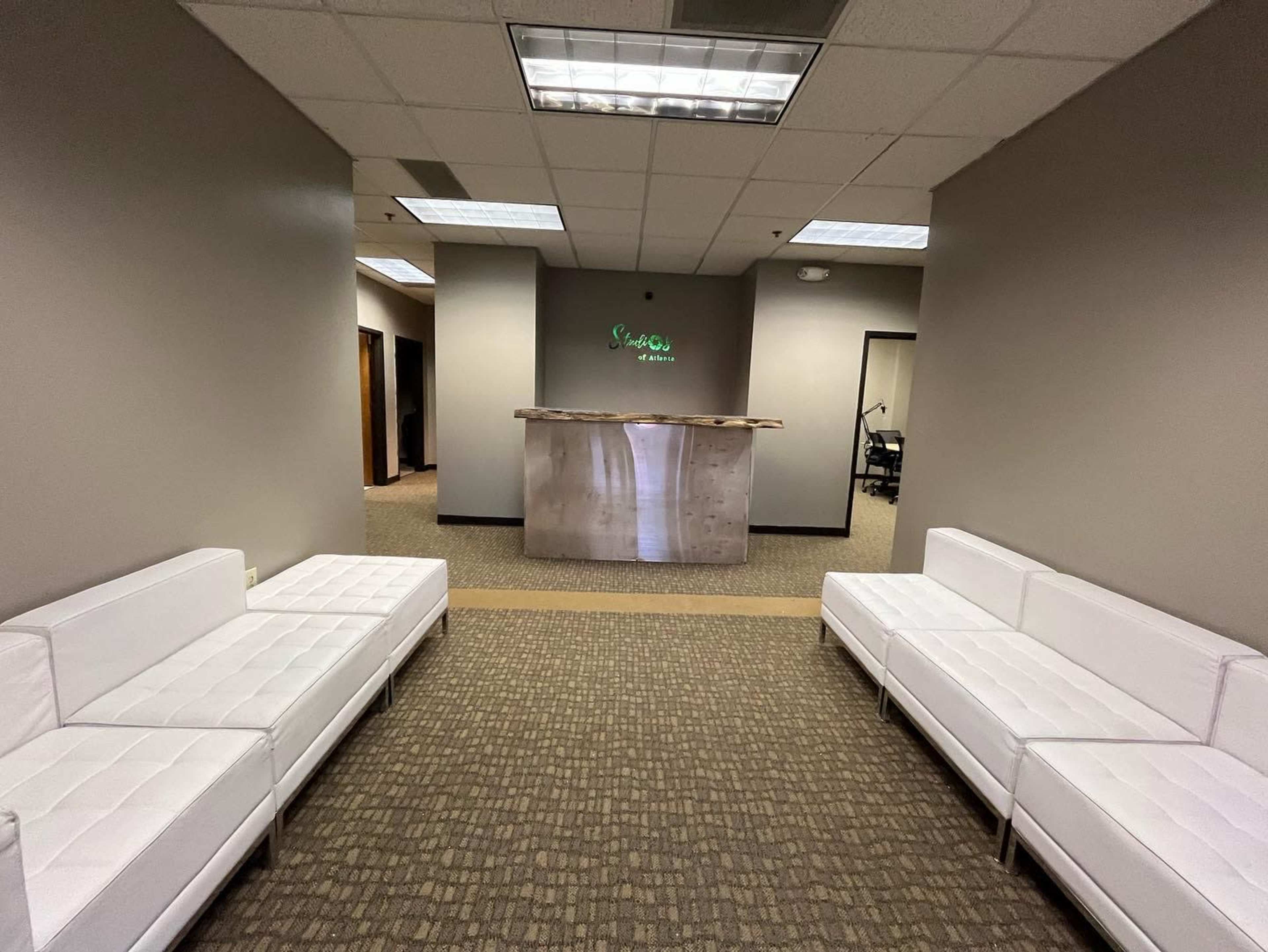 A waiting area with two white sofas facing a reception desk in a modern office environment.