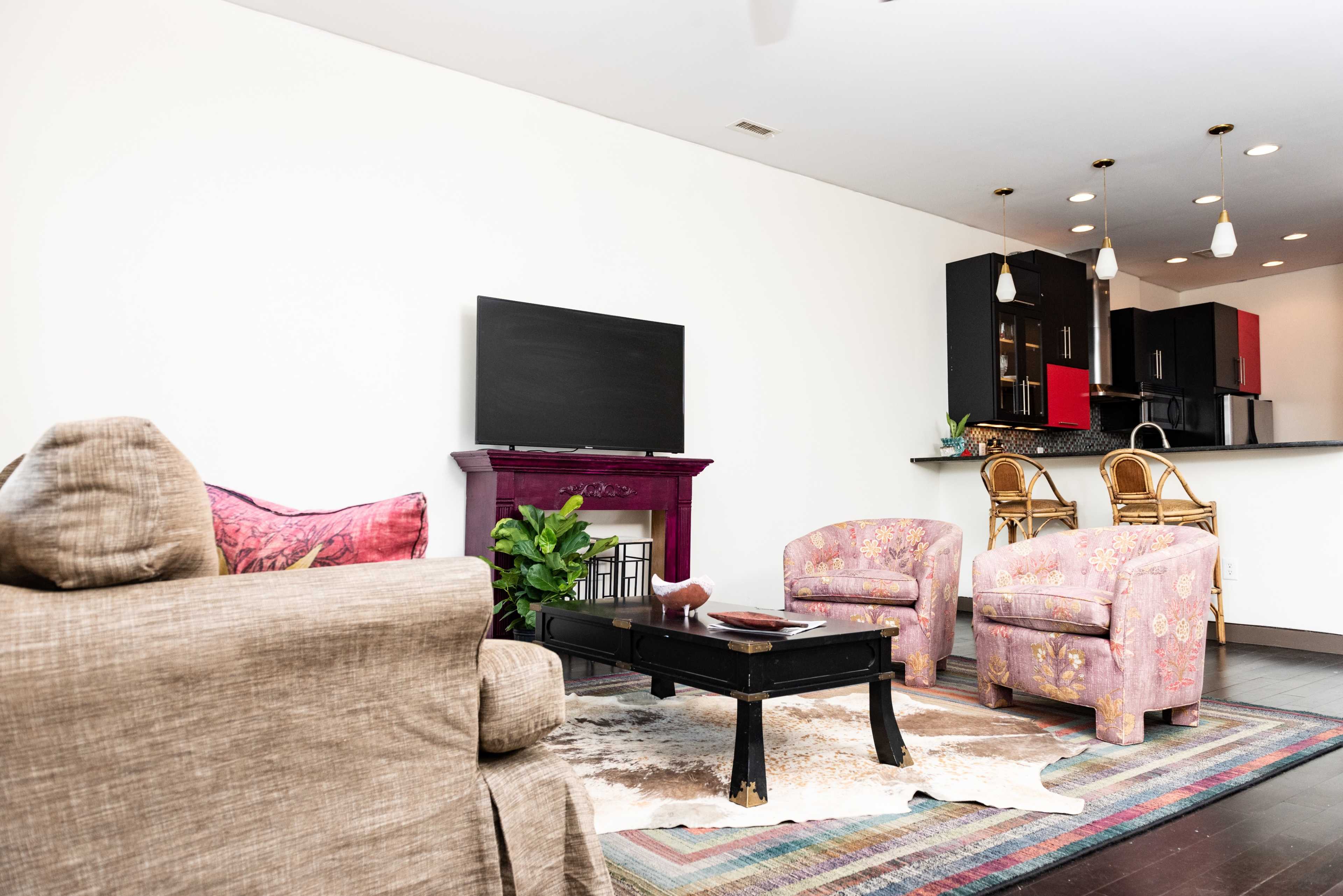 A modern living room with a television, a purple fireplace, and colorful chairs, leading to an open kitchen area.