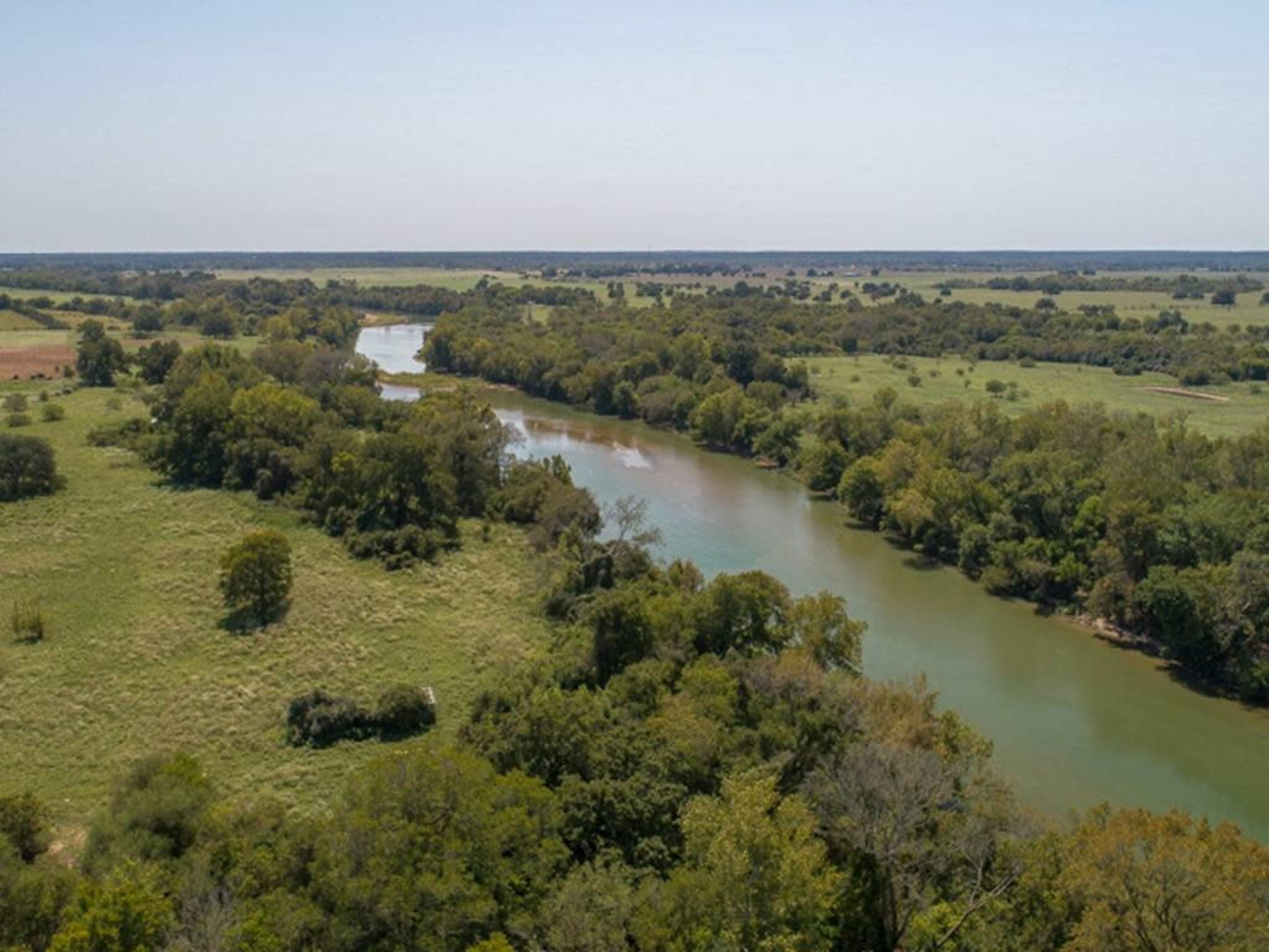 A wide river flows through a lush green landscape dotted with trees and fields.