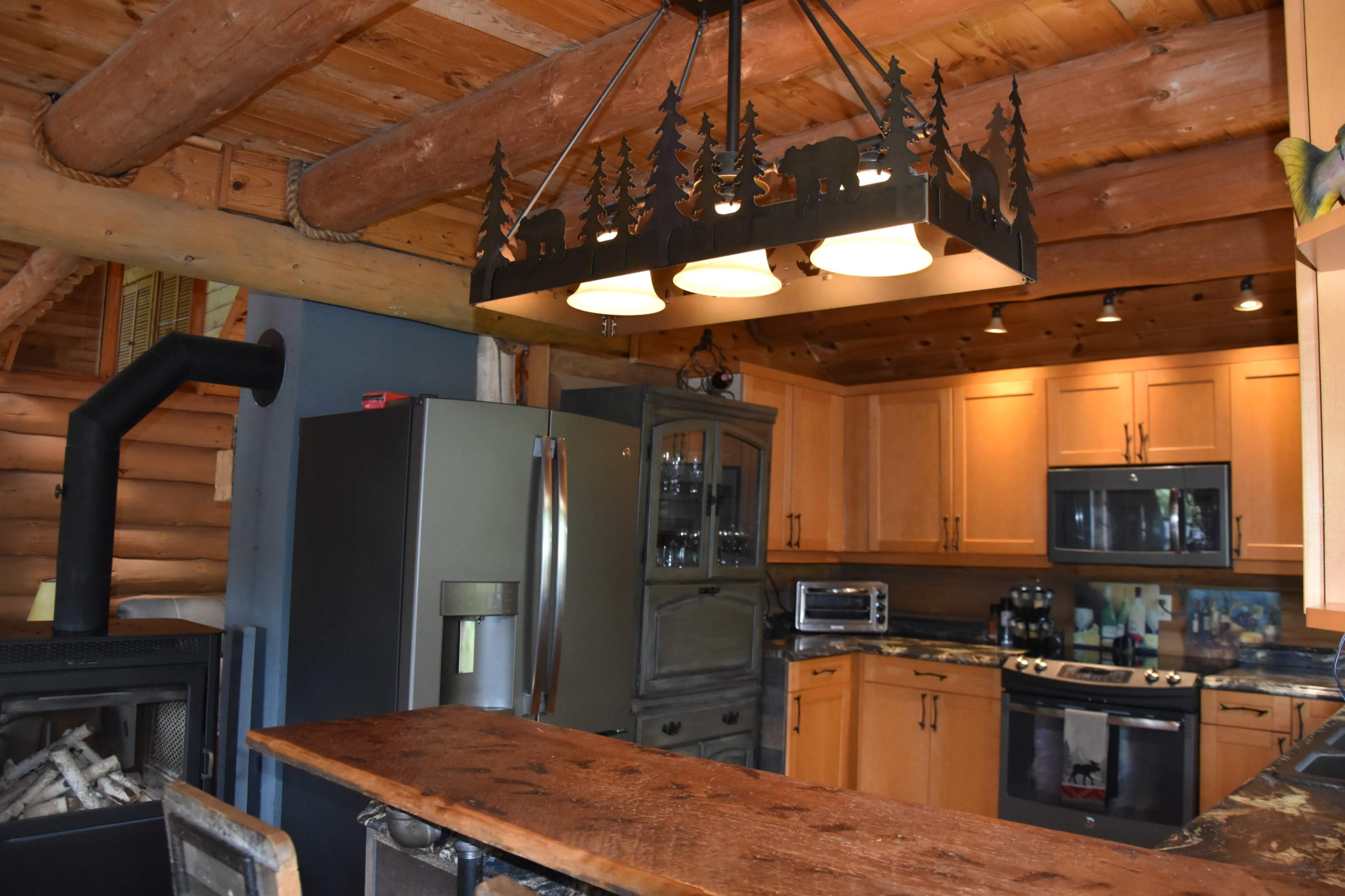 A rustic kitchen featuring wooden cabinets, a central island with a wooden countertop, and a light fixture resembling trees and a bear overhead.