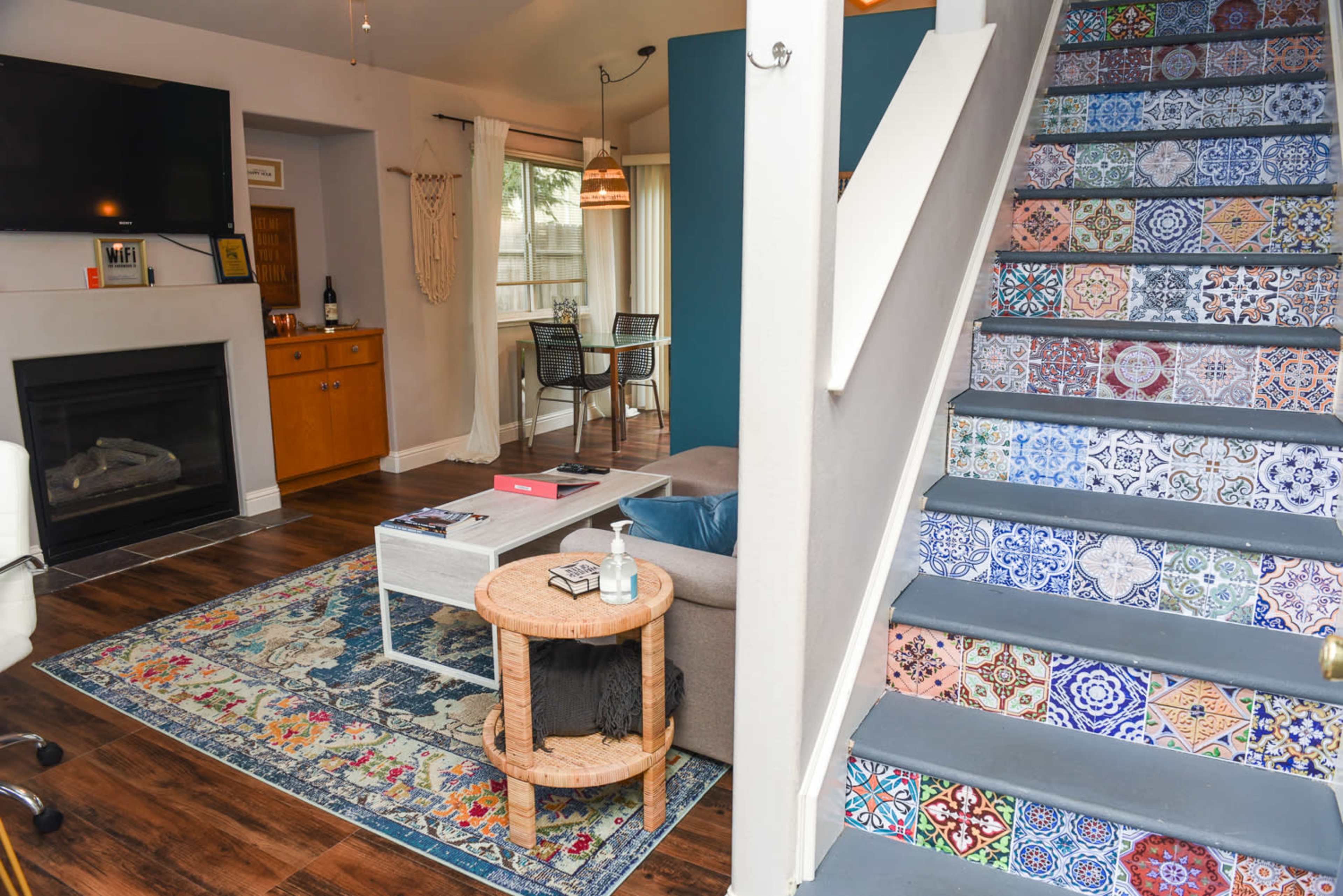 The image shows a living room with a fireplace, a couch, a coffee table, and a staircase featuring colorful patterned tiles.