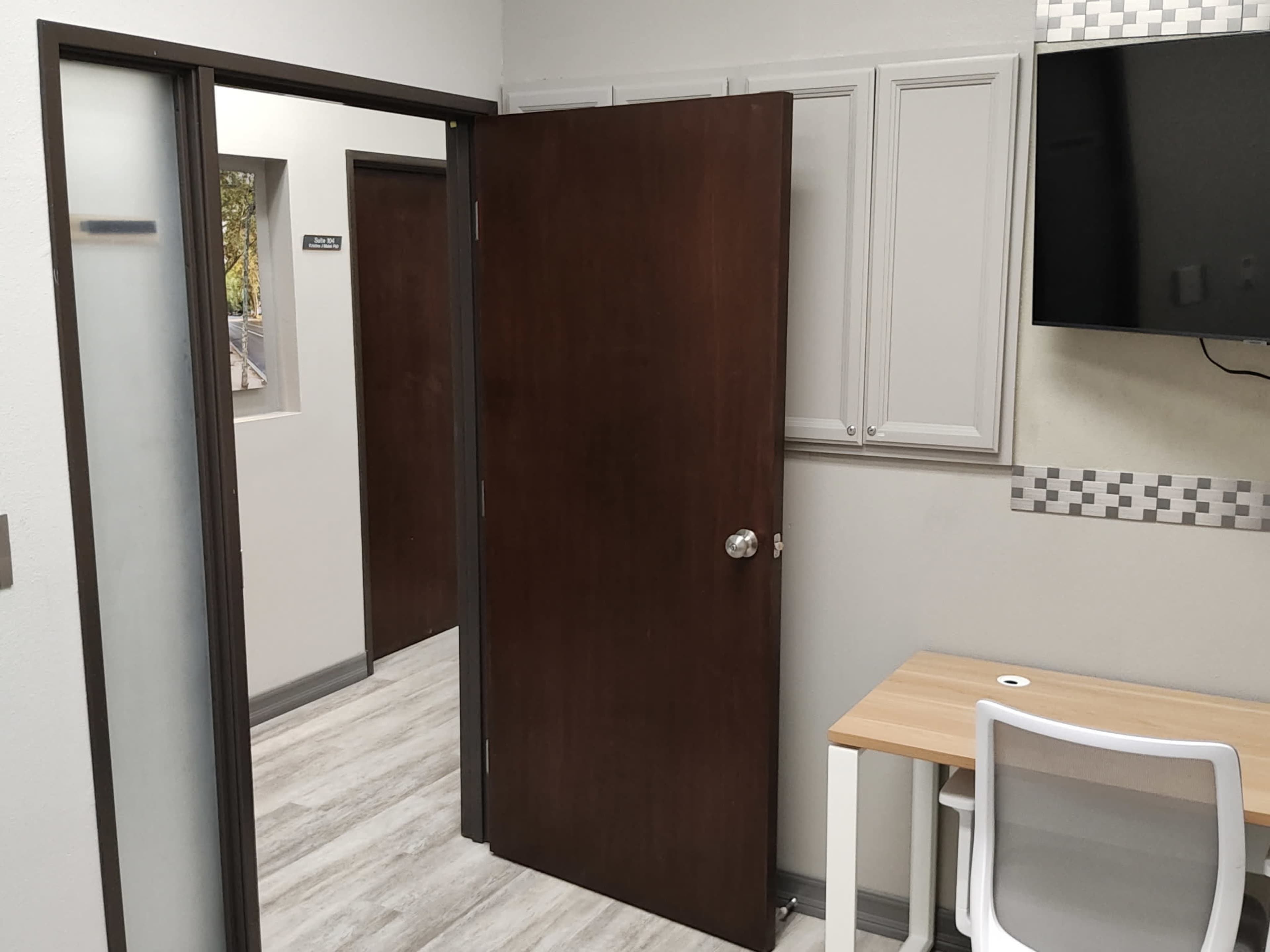 The image shows an interior office space with an open door leading to another room and a desk with a chair against a wall.