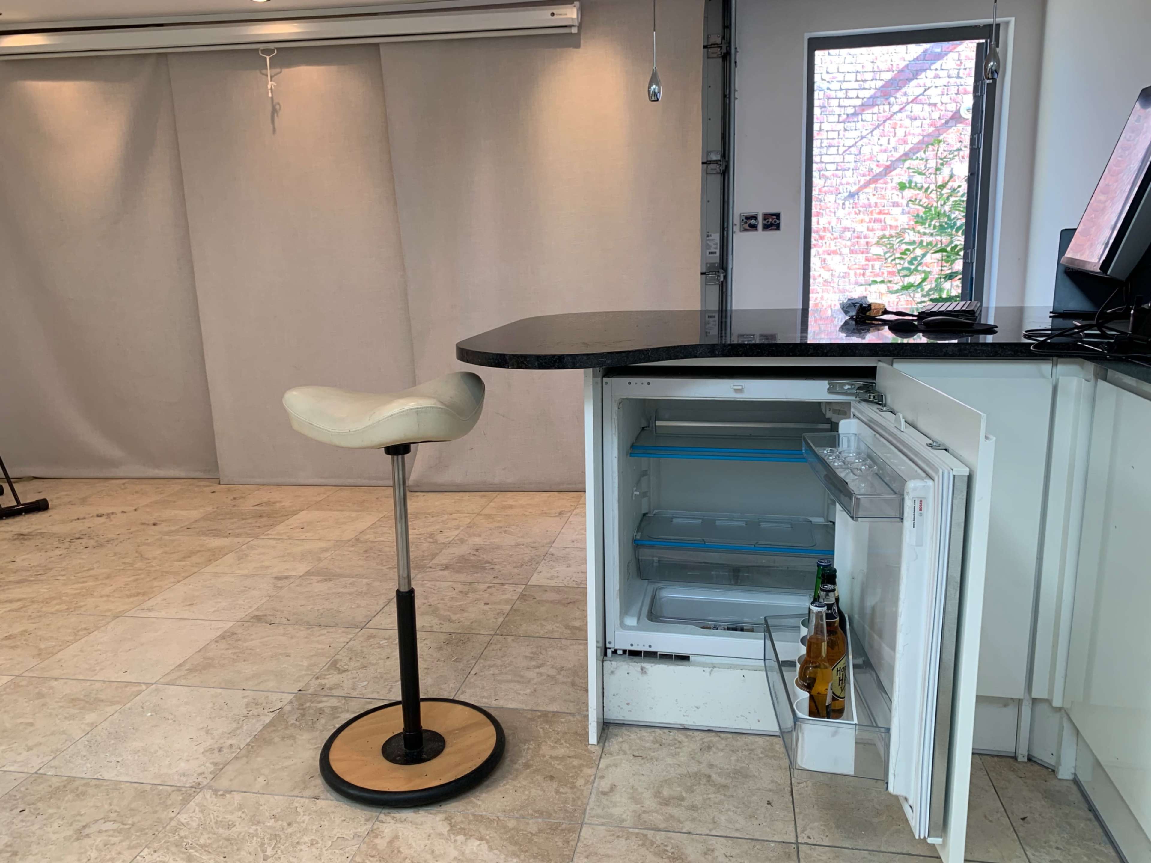 A kitchen space featuring a black countertop with a single stool and an open refrigerator, adjacent to a window.