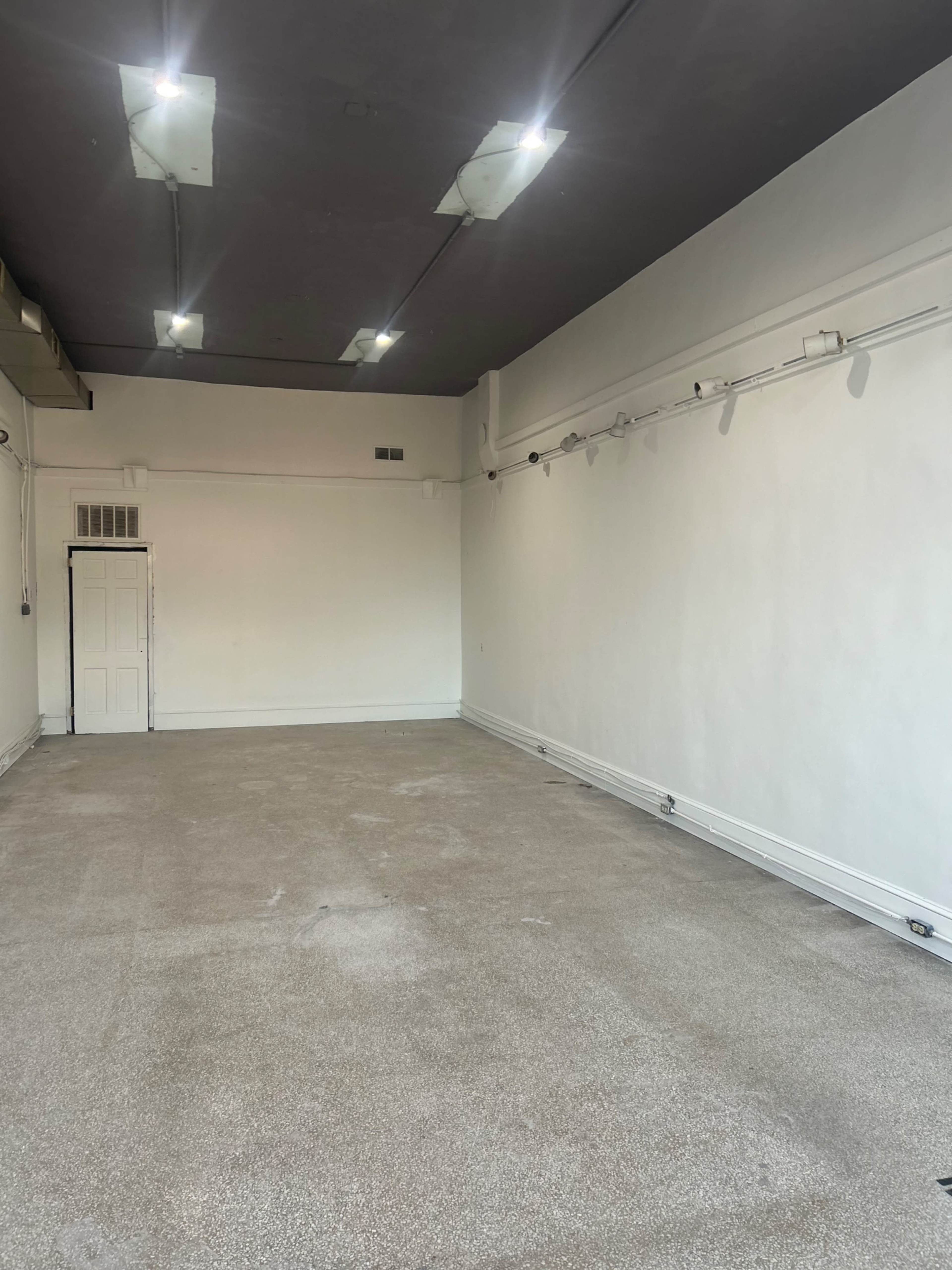 The image shows an empty room with light-colored walls, a bare floor, and several ceiling lights.
