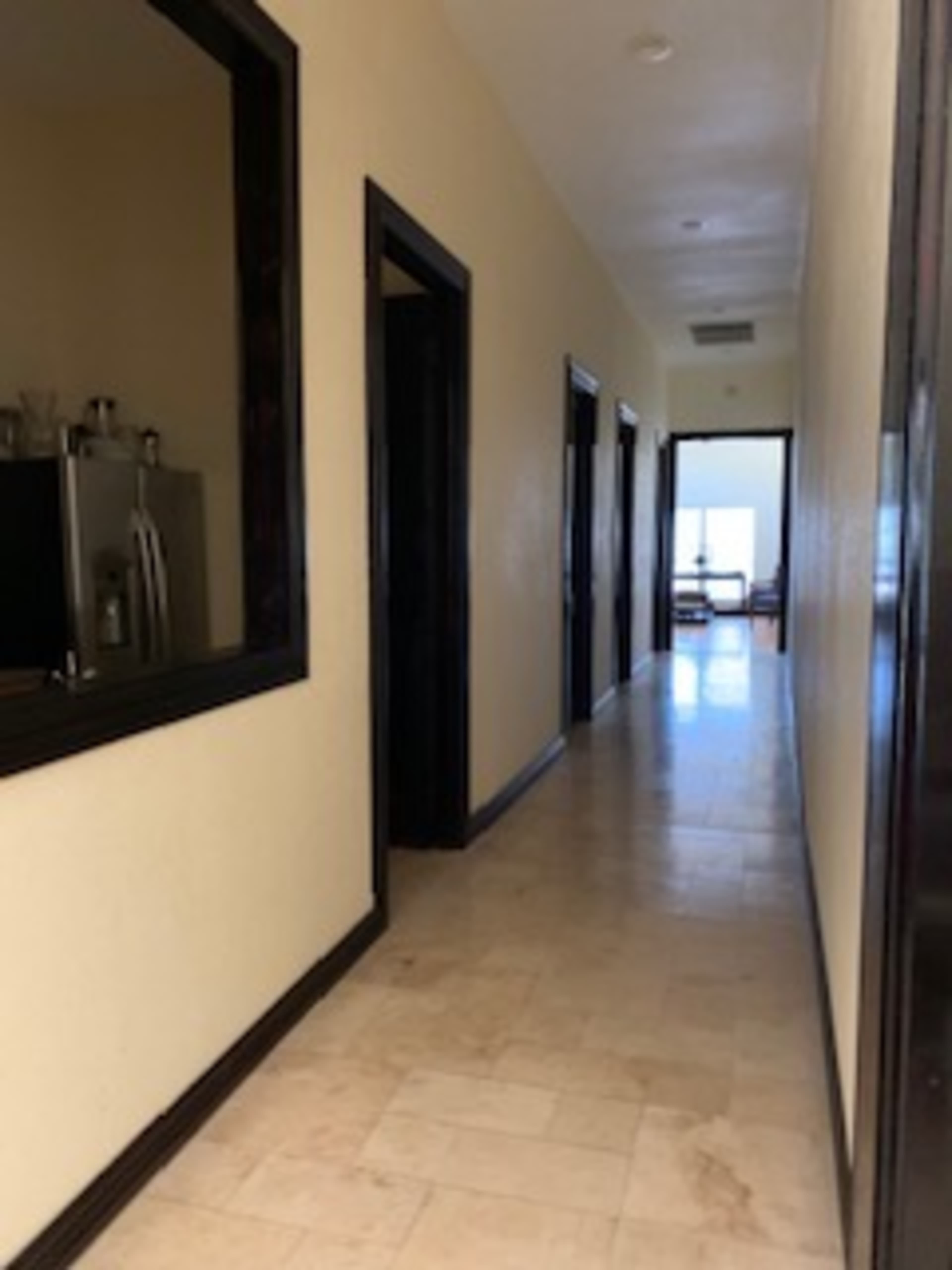 A long hallway with doorways on either side and a view of a room at the end.