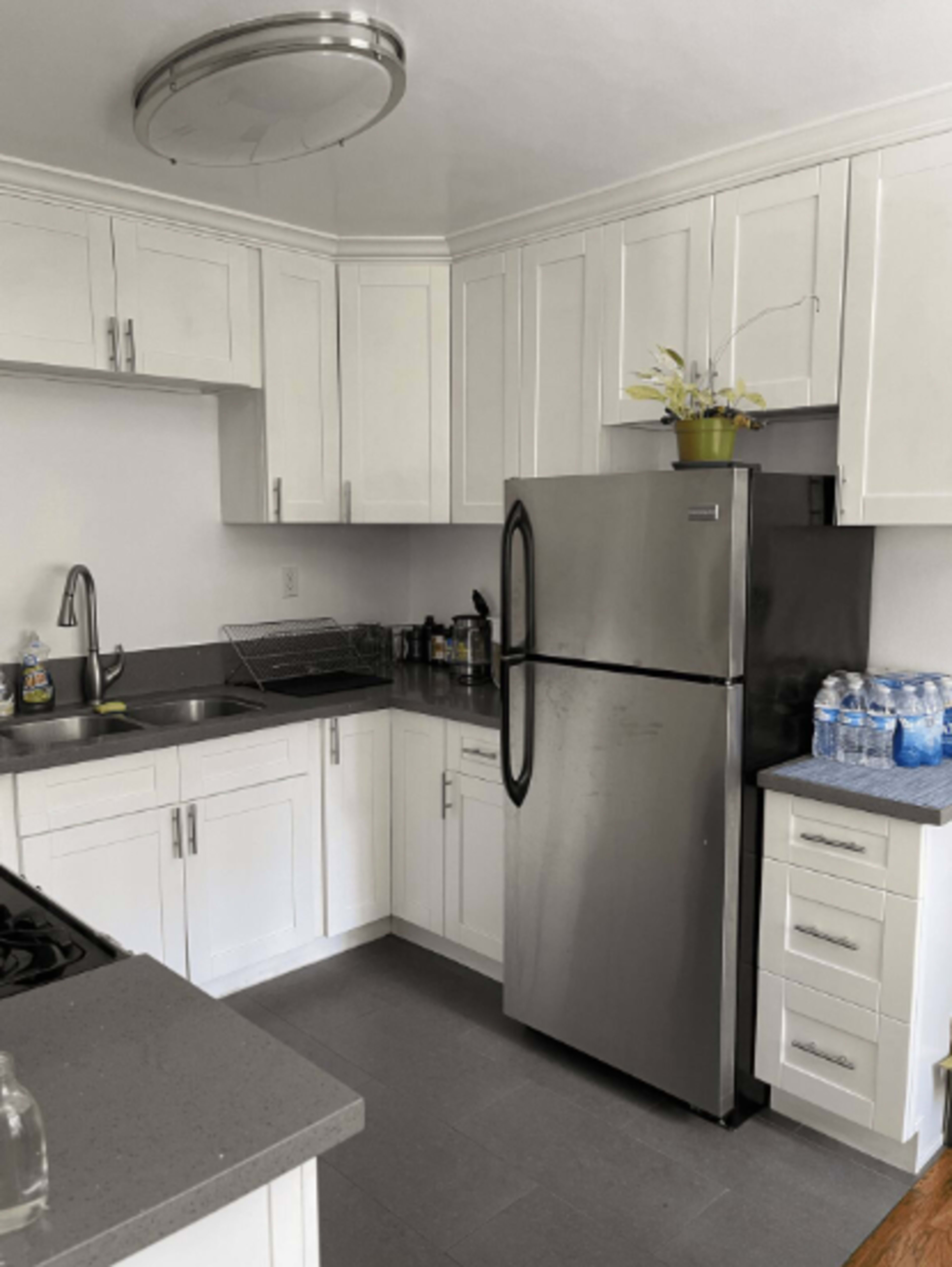 A modern kitchen featuring white cabinets, a stainless steel refrigerator, a sink, and a countertop with water bottles.