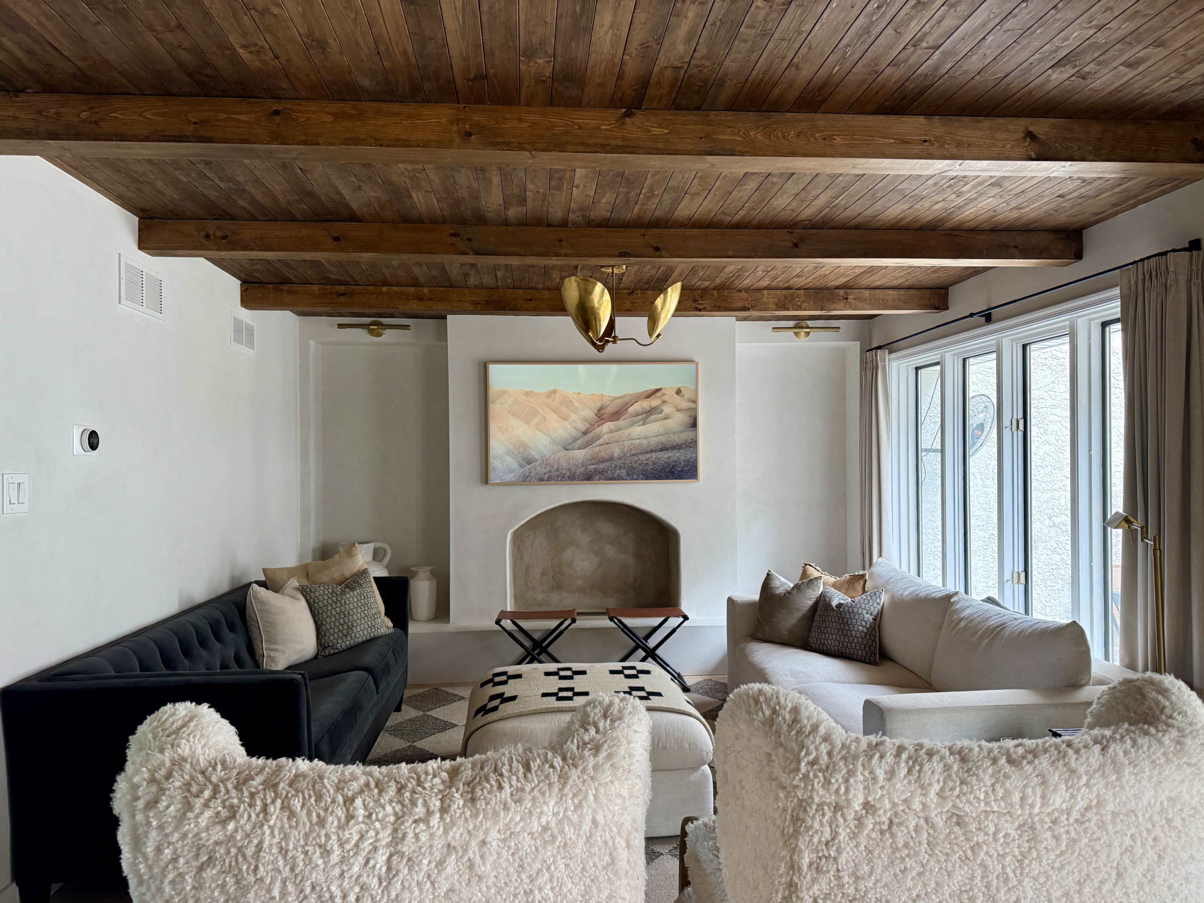 The room features a cozy sitting area with two sofas, a coffee table, and a large piece of artwork above a fireplace, all under a wooden beamed ceiling.