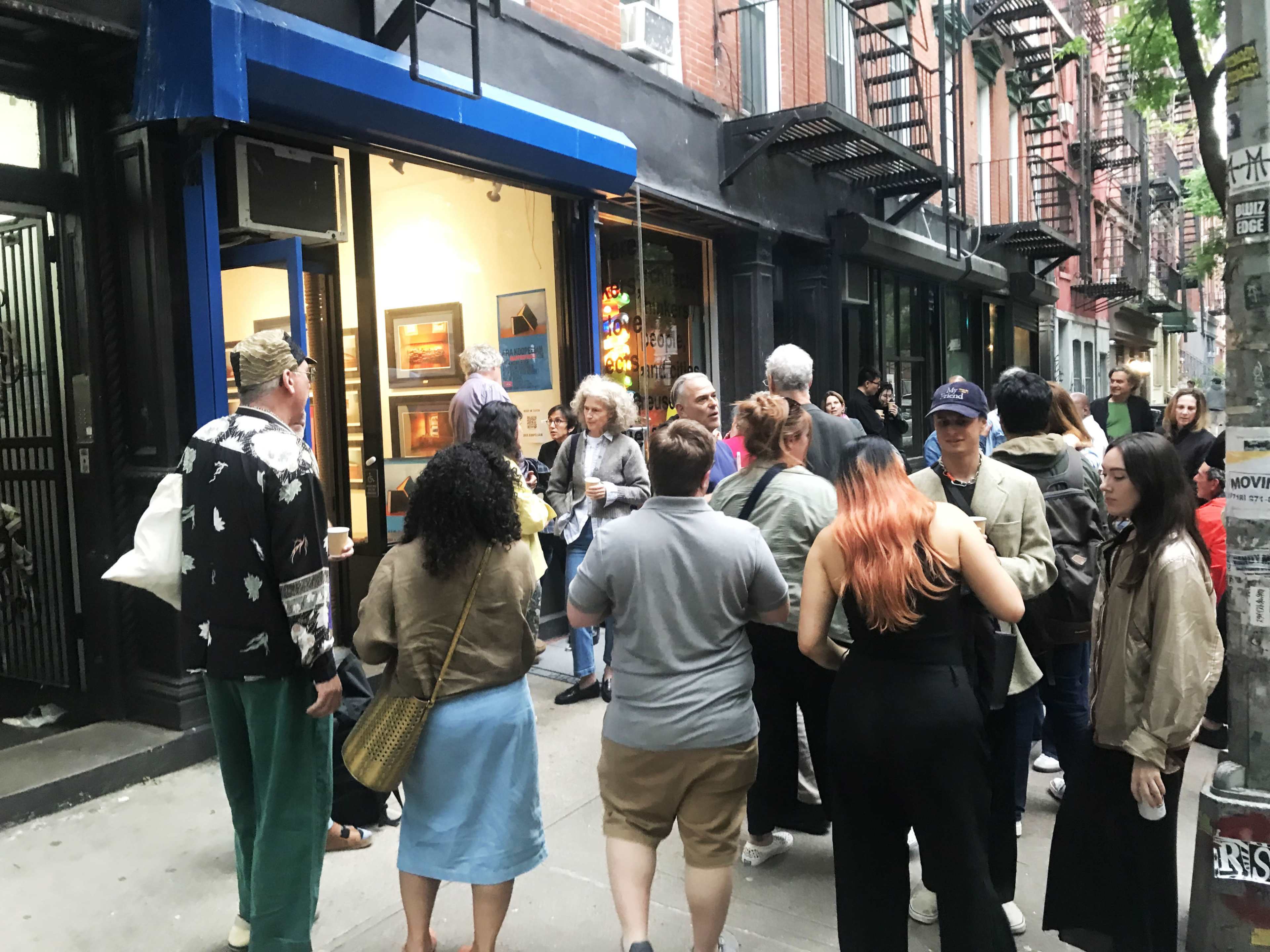 A group of people gathers outside an art gallery on a busy city street.