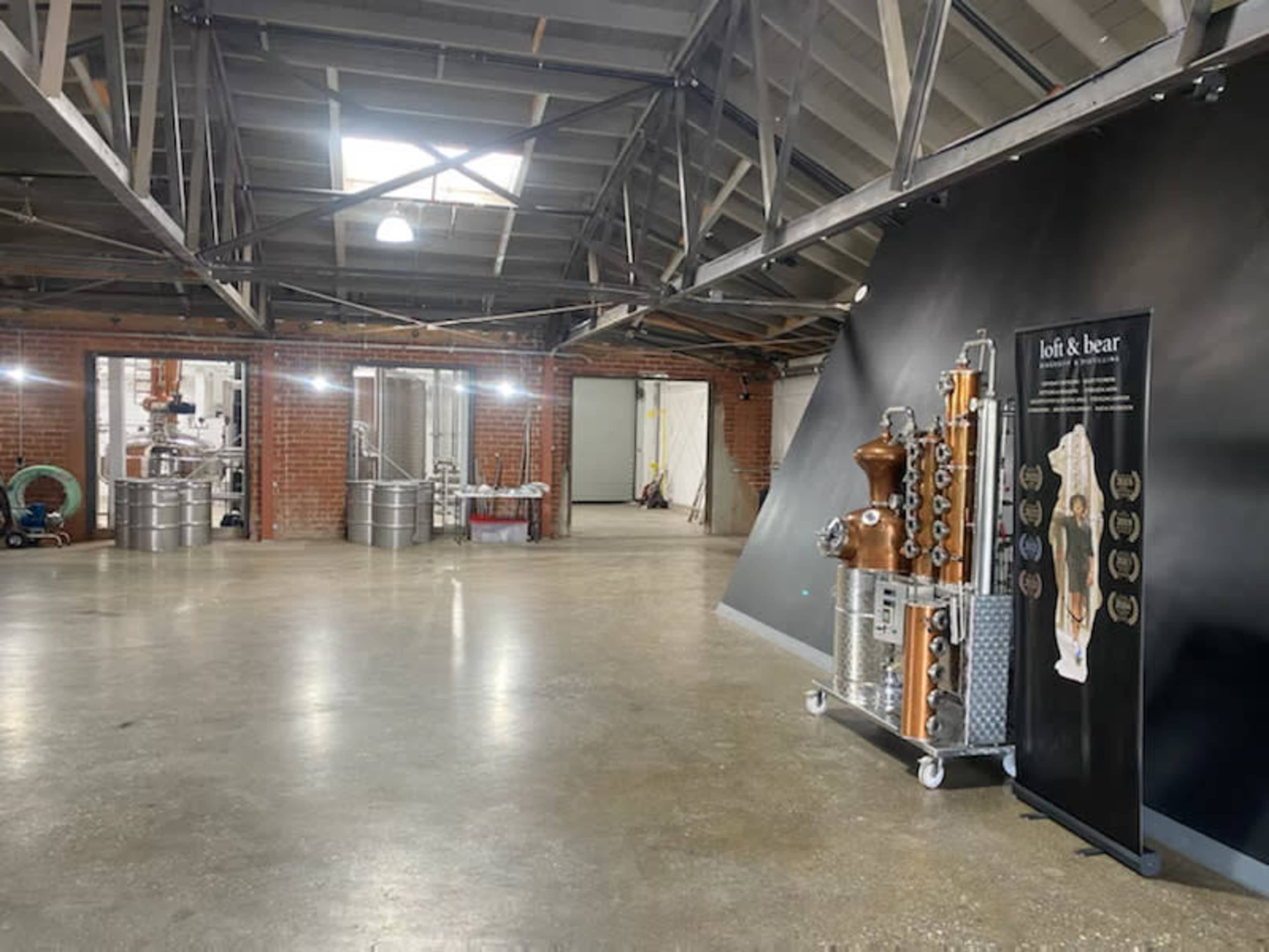 An industrial space with polished concrete floors, exposed beams, and a display featuring distillation equipment alongside large metal tanks in the background.