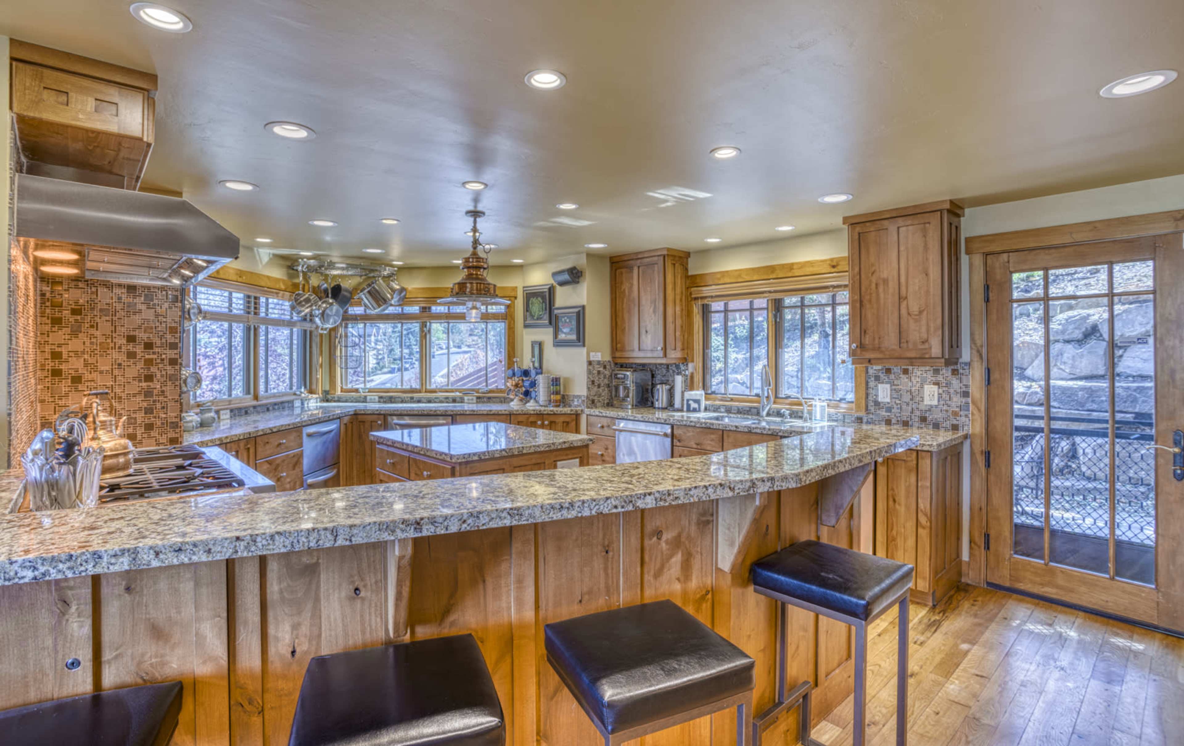 The kitchen features a large granite countertop with bar seating, wooden cabinetry, and multiple windows providing natural light and a view of the outdoors.