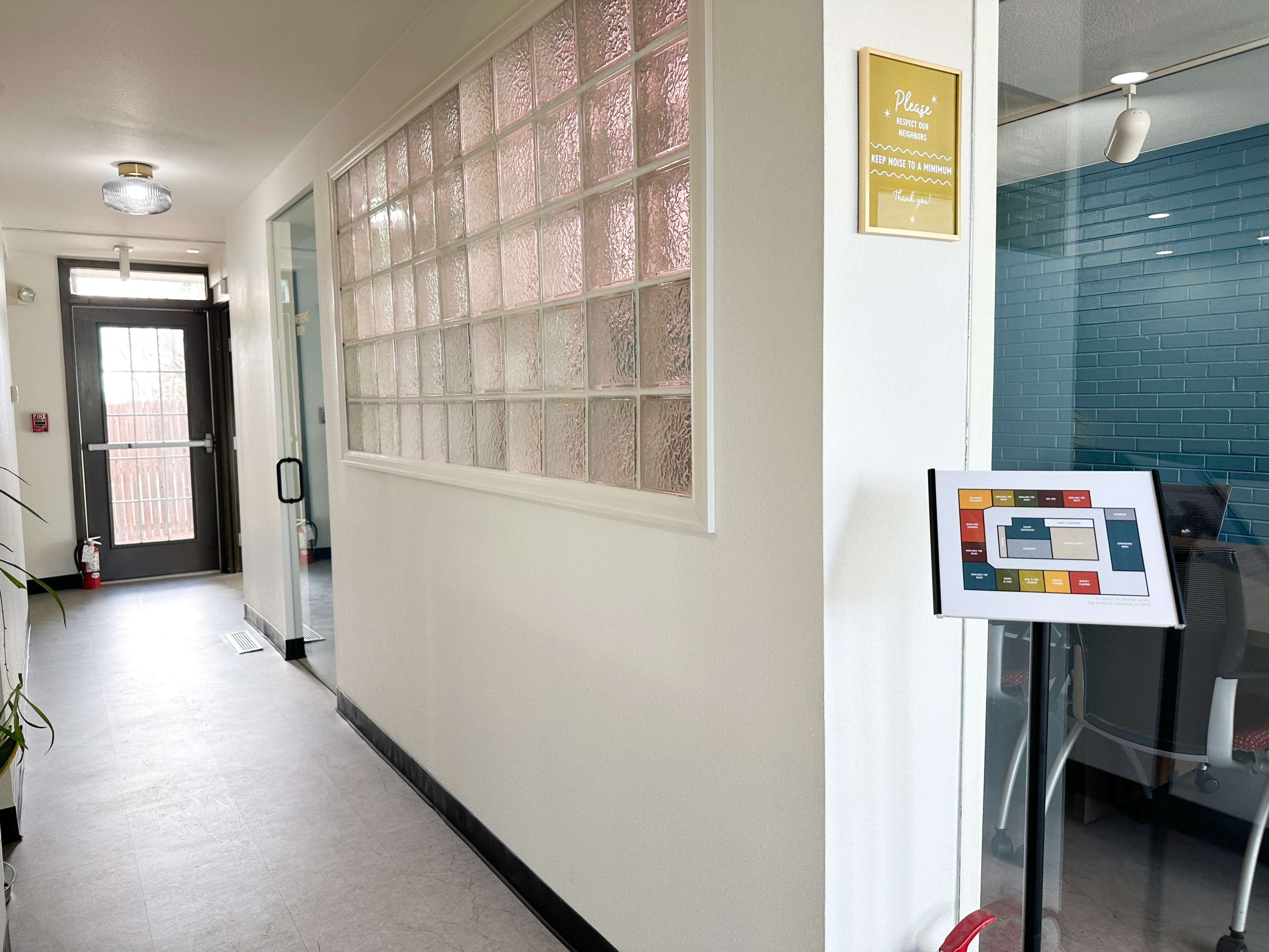 The image shows a hallway with a glass block wall to the left, leading to a door at the end and a digital display panel on the right.