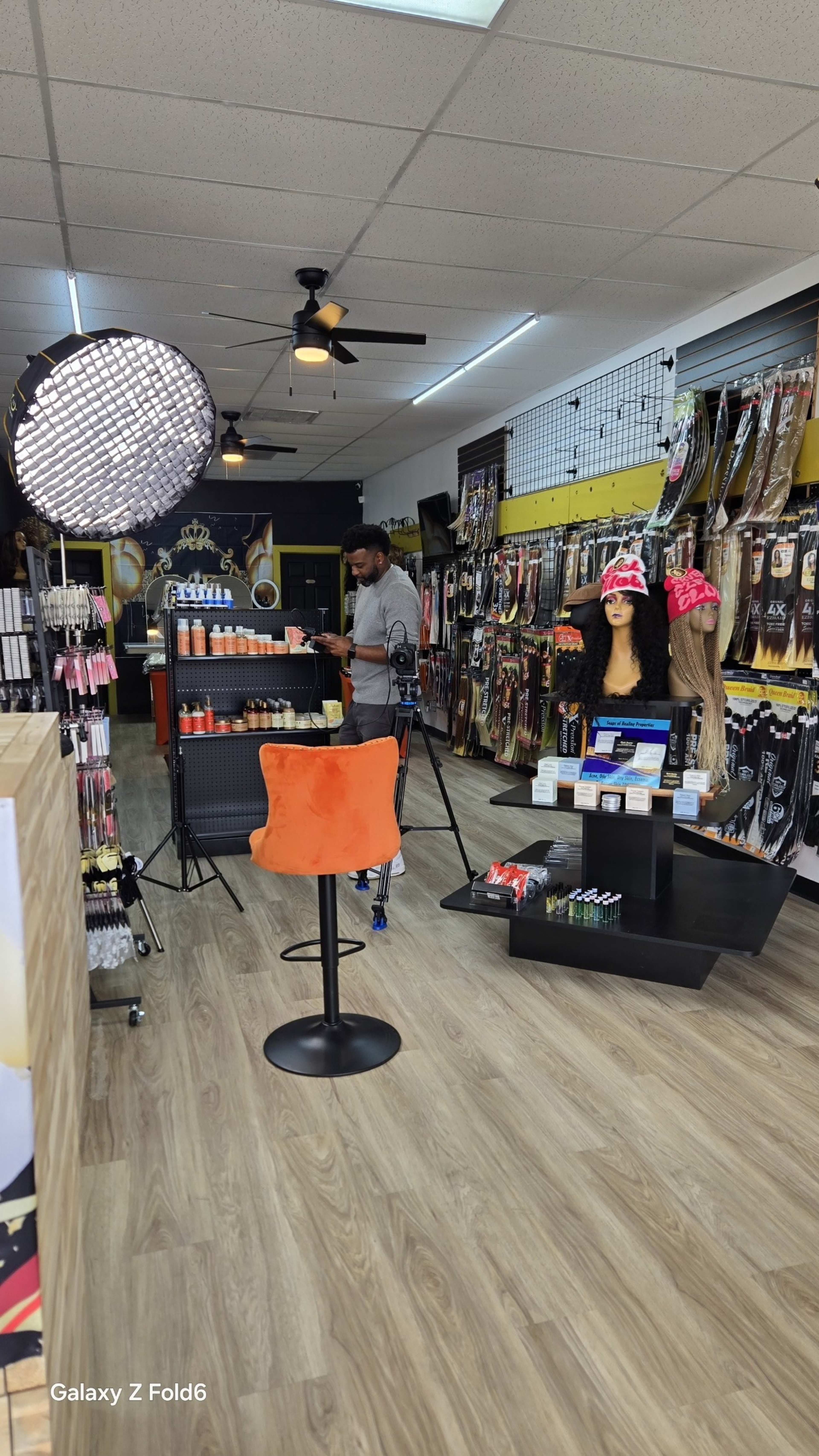 A man sets up a photography backdrop in a hair and beauty supply store filled with various hair products and accessories.