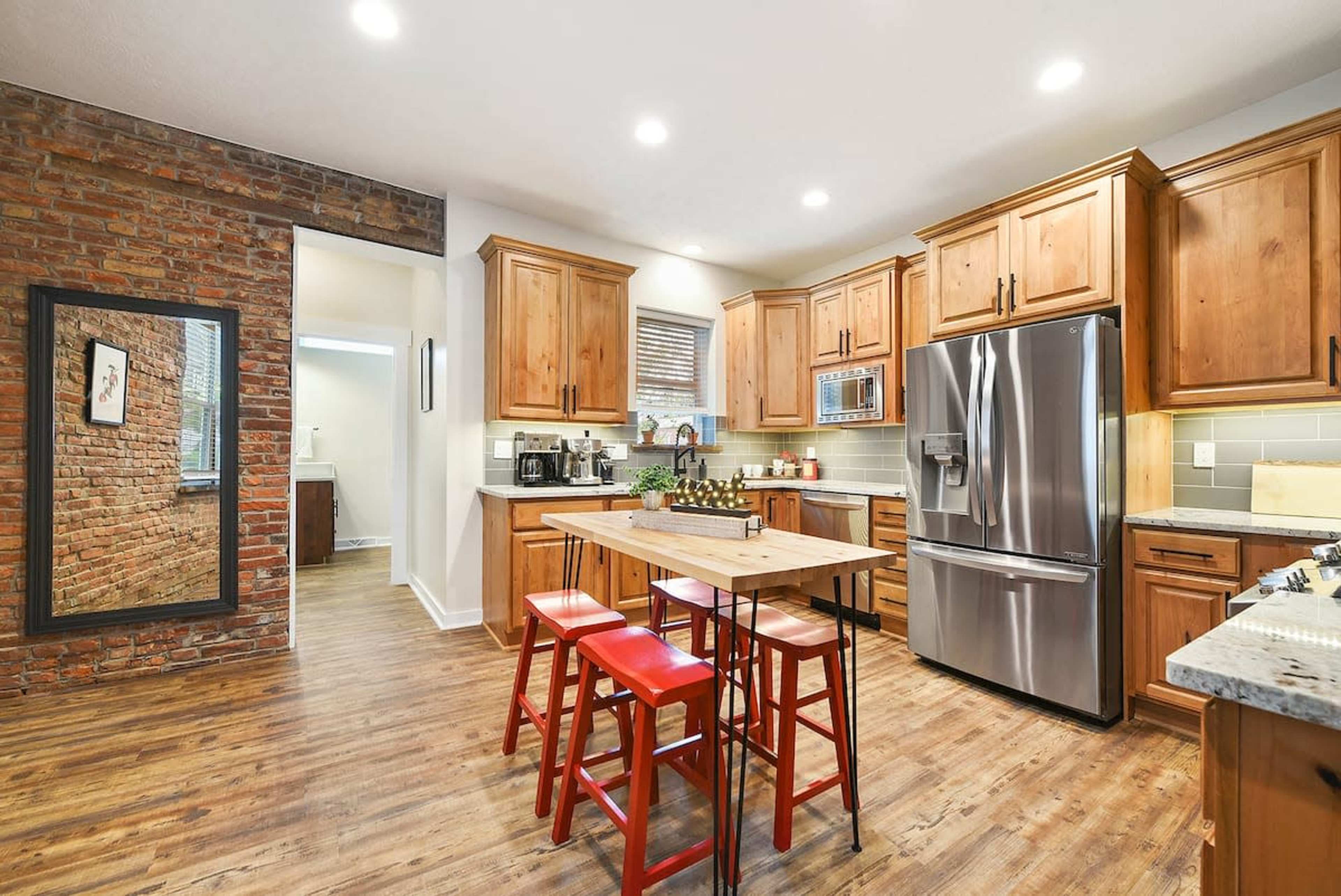 A modern kitchen features wooden cabinetry, stainless steel appliances, and a central island with red stools.