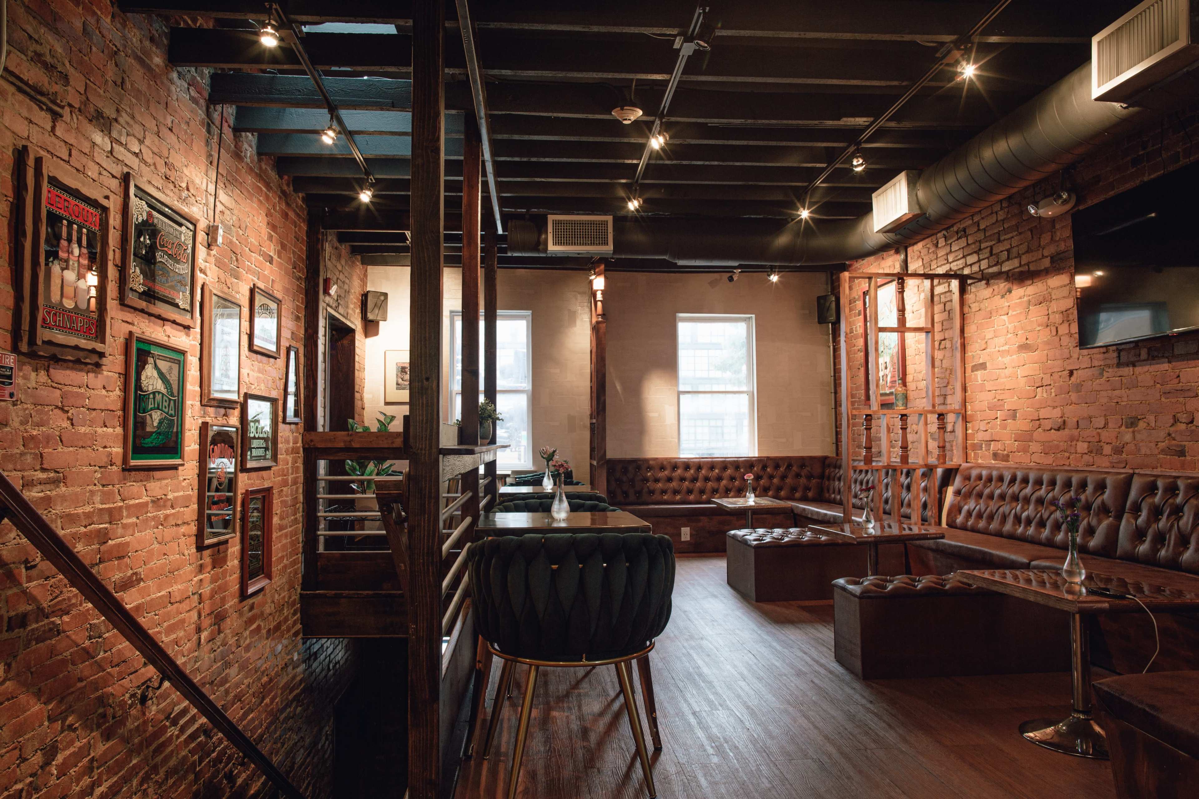 The interior of a restaurant features exposed brick walls, wooden beams, and a mix of leather seating and modern decor.