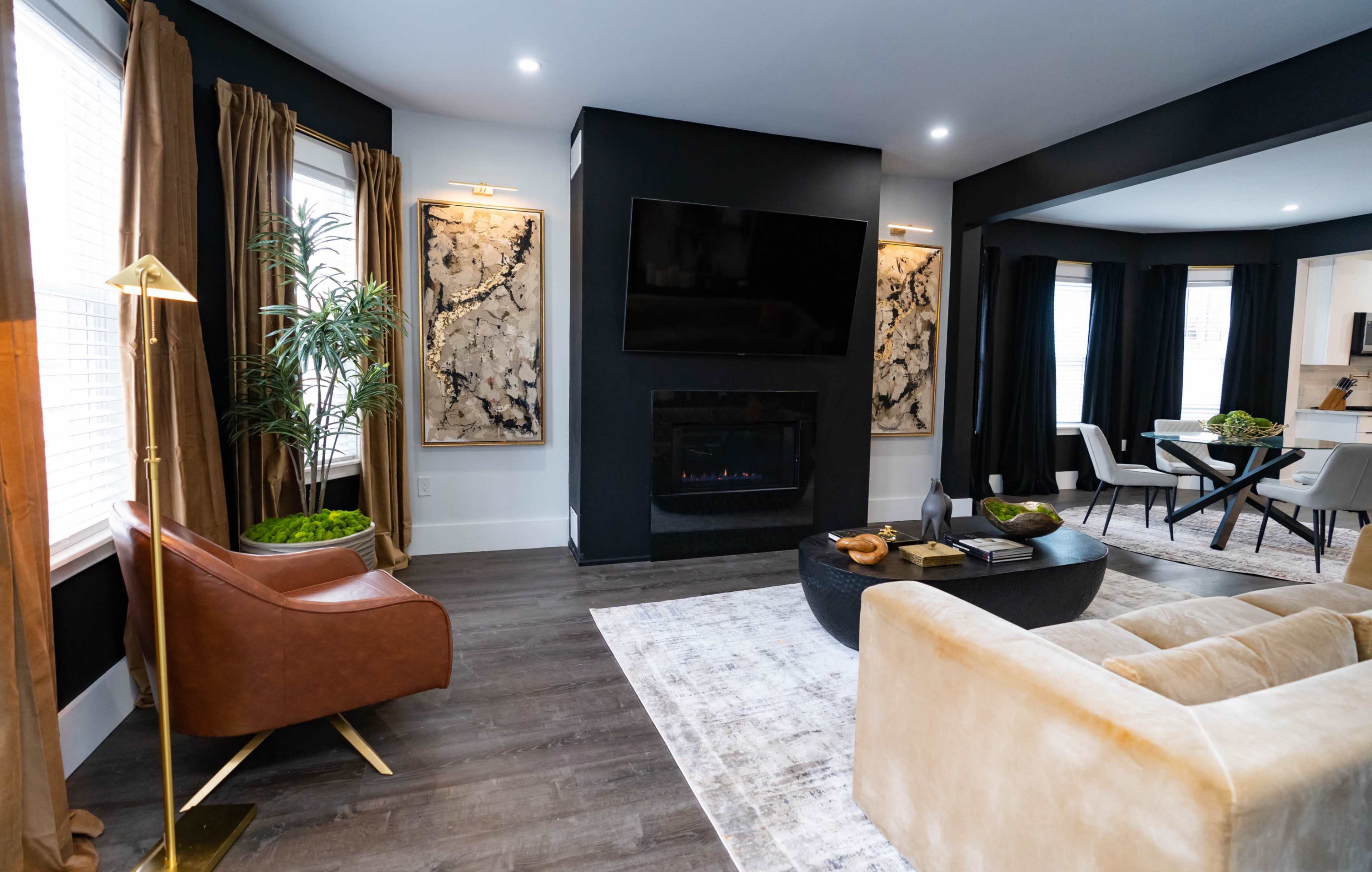 The living room features a modern seating arrangement with a plush sofa, an accent chair, and a wall-mounted television, complemented by a fireplace and decorative artwork.