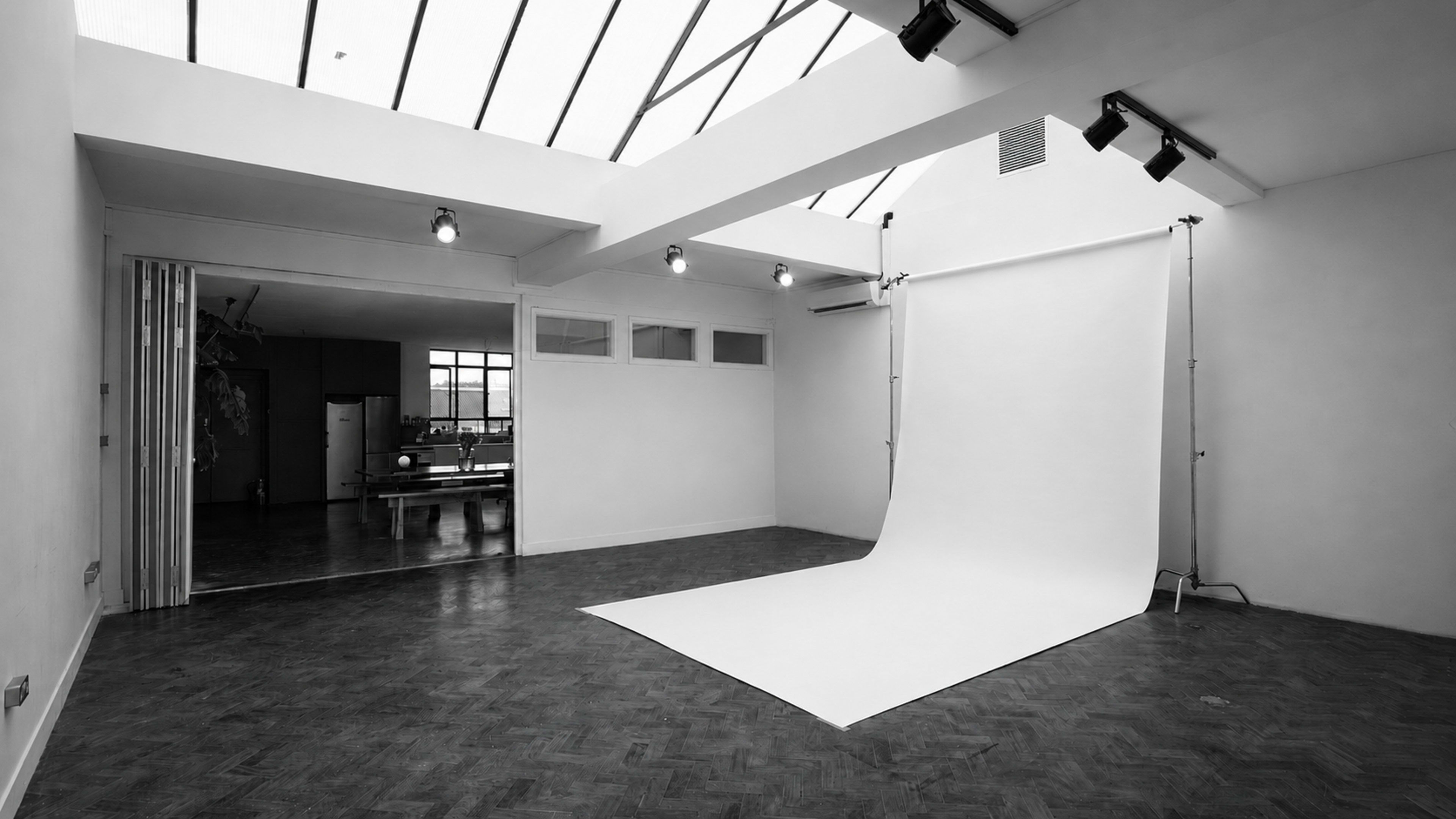 The image shows a spacious photography studio with a white backdrop and large windows allowing natural light.