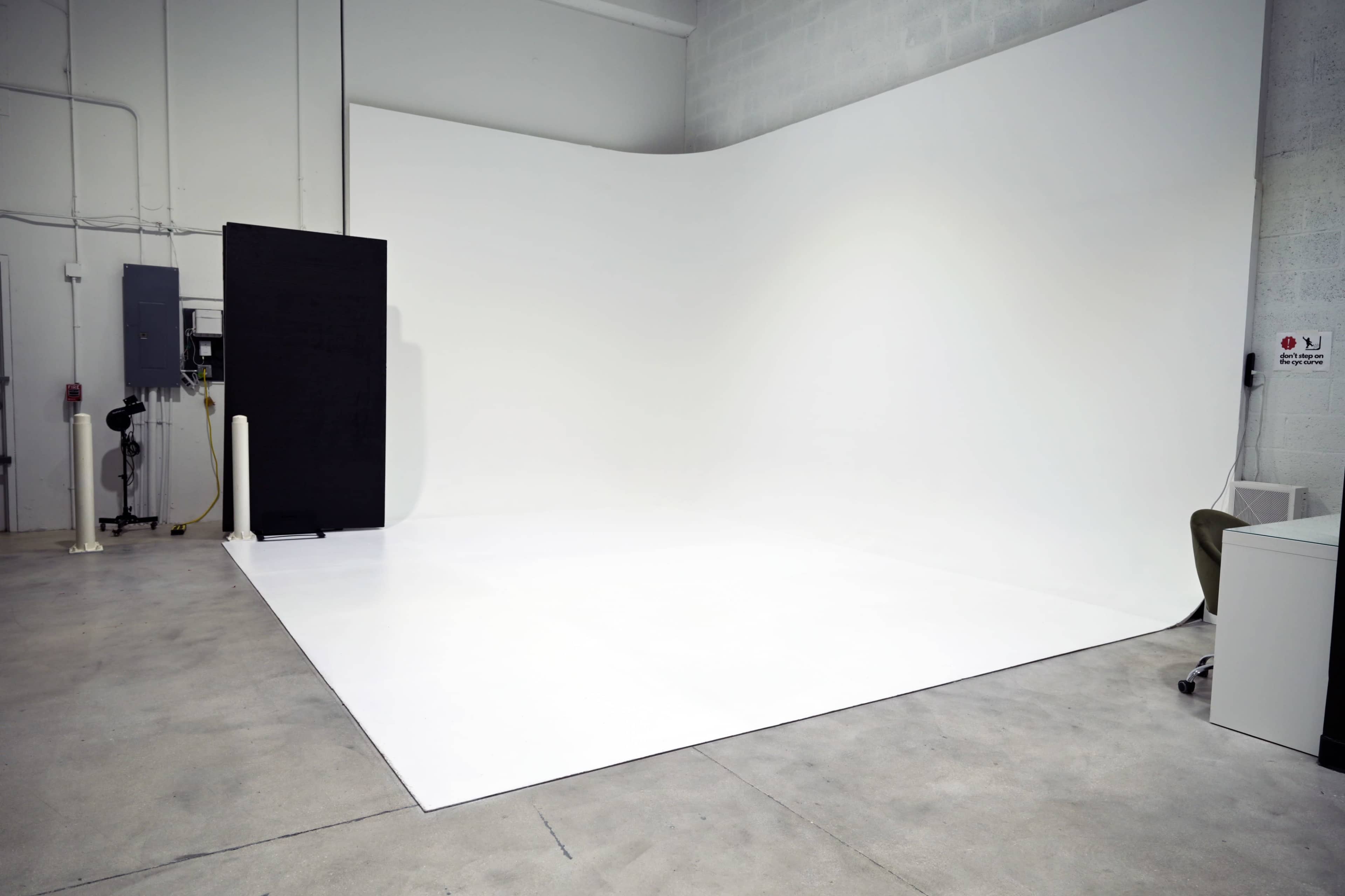 The image shows a spacious, empty studio with a white backdrop and a smooth concrete floor.