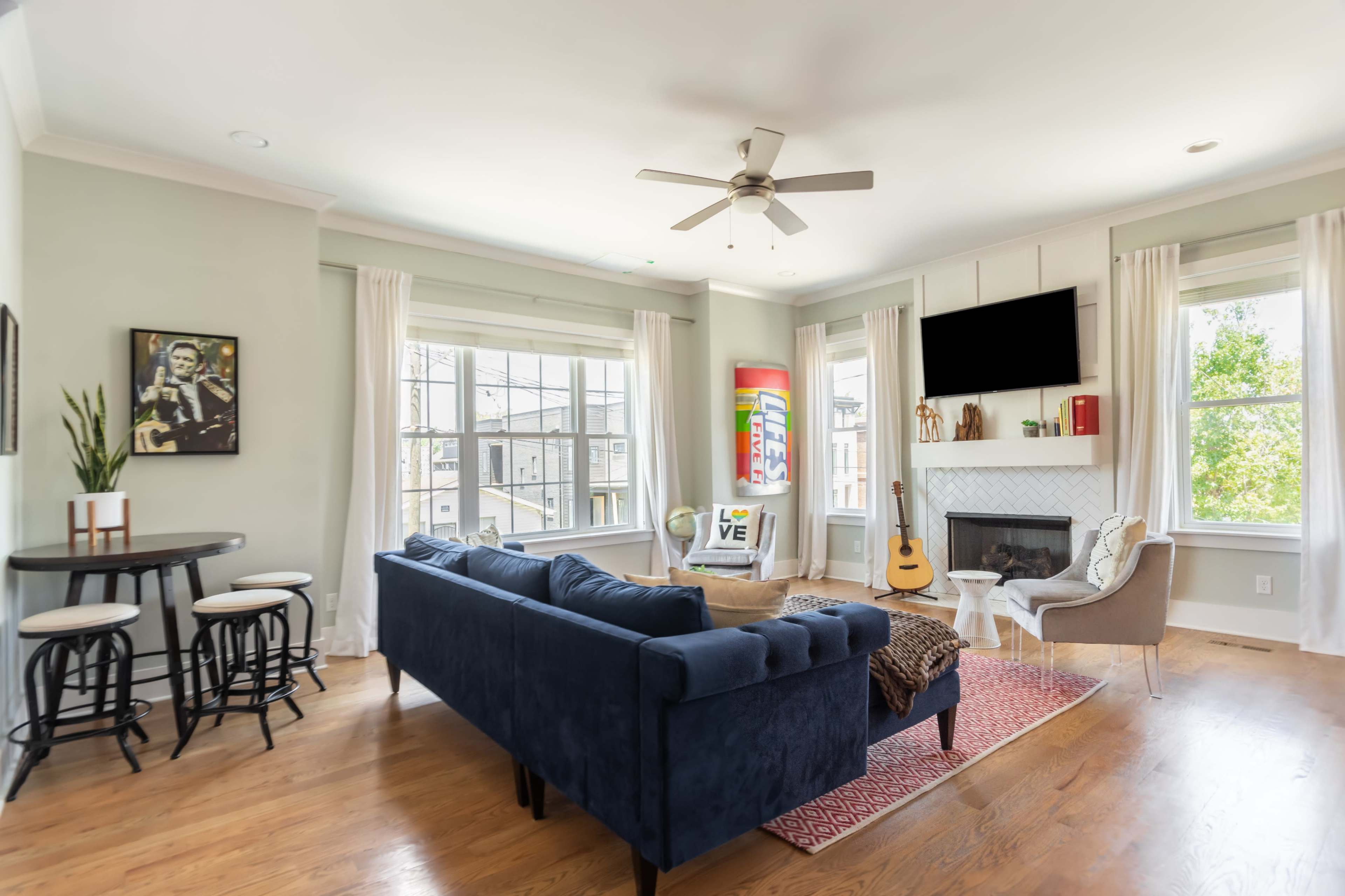 The living room features a blue couch, a round dining table, a fireplace, and large windows that provide natural light.