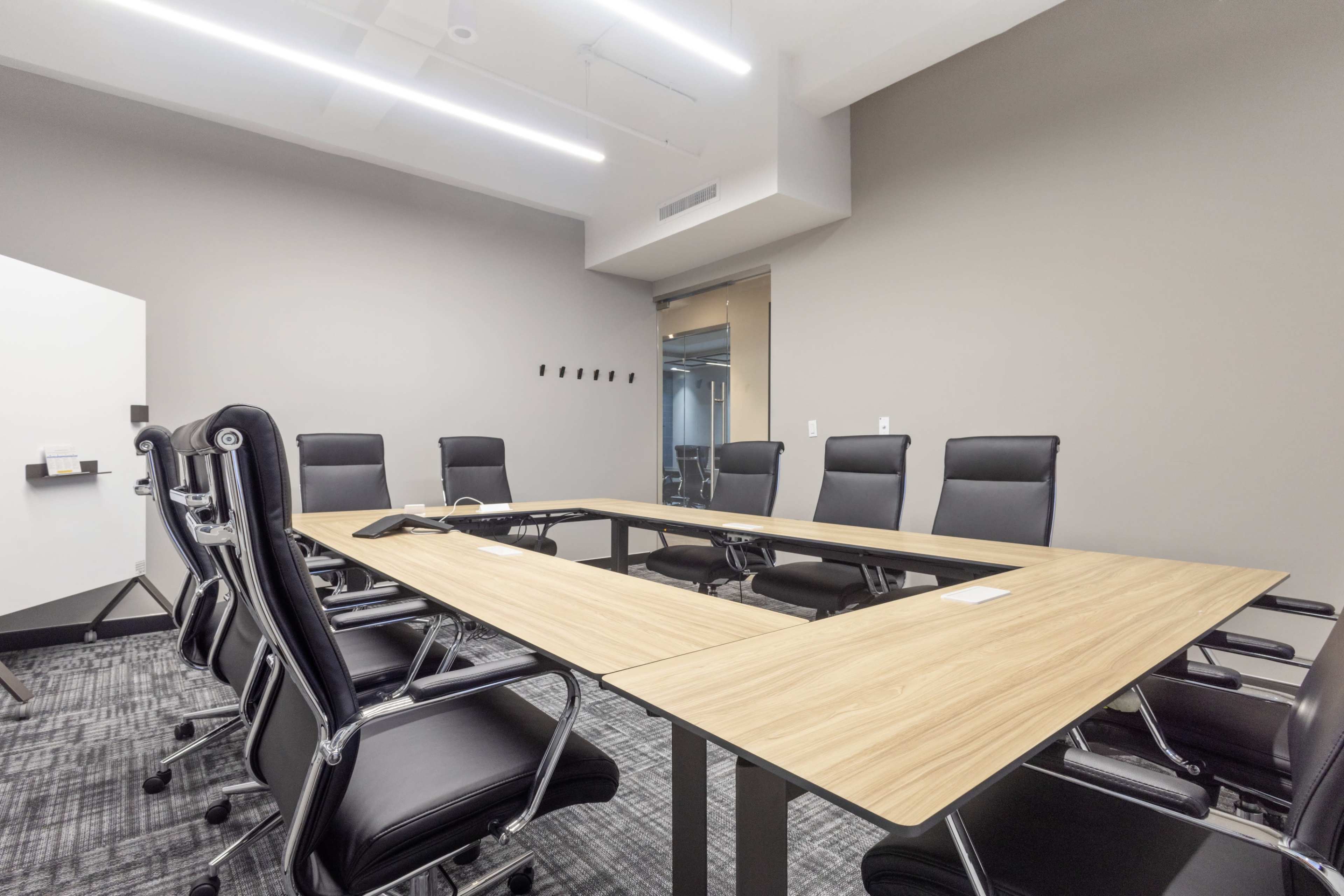 A modern conference room features a large wooden table surrounded by eight black ergonomic chairs.