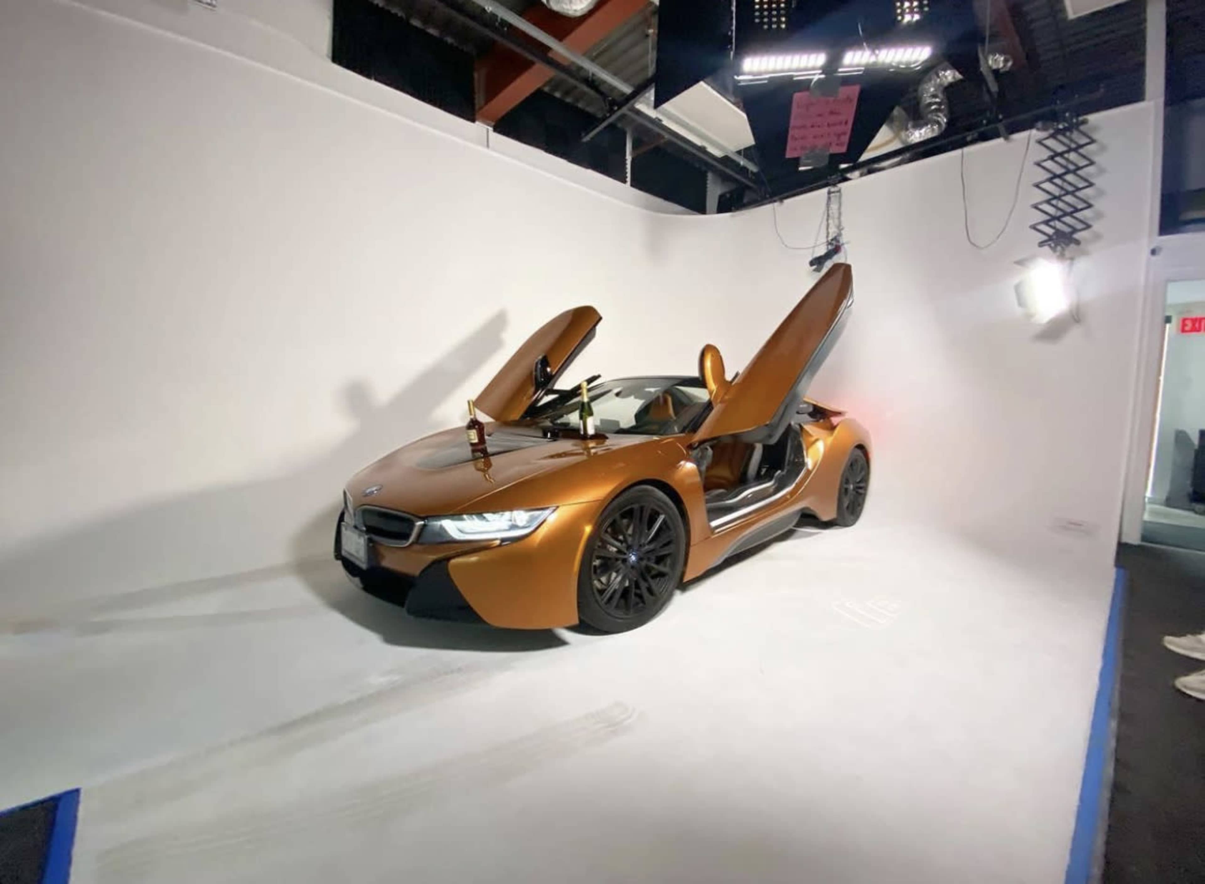 A BMW i8 with its doors open is displayed against a plain white backdrop in a studio setting.