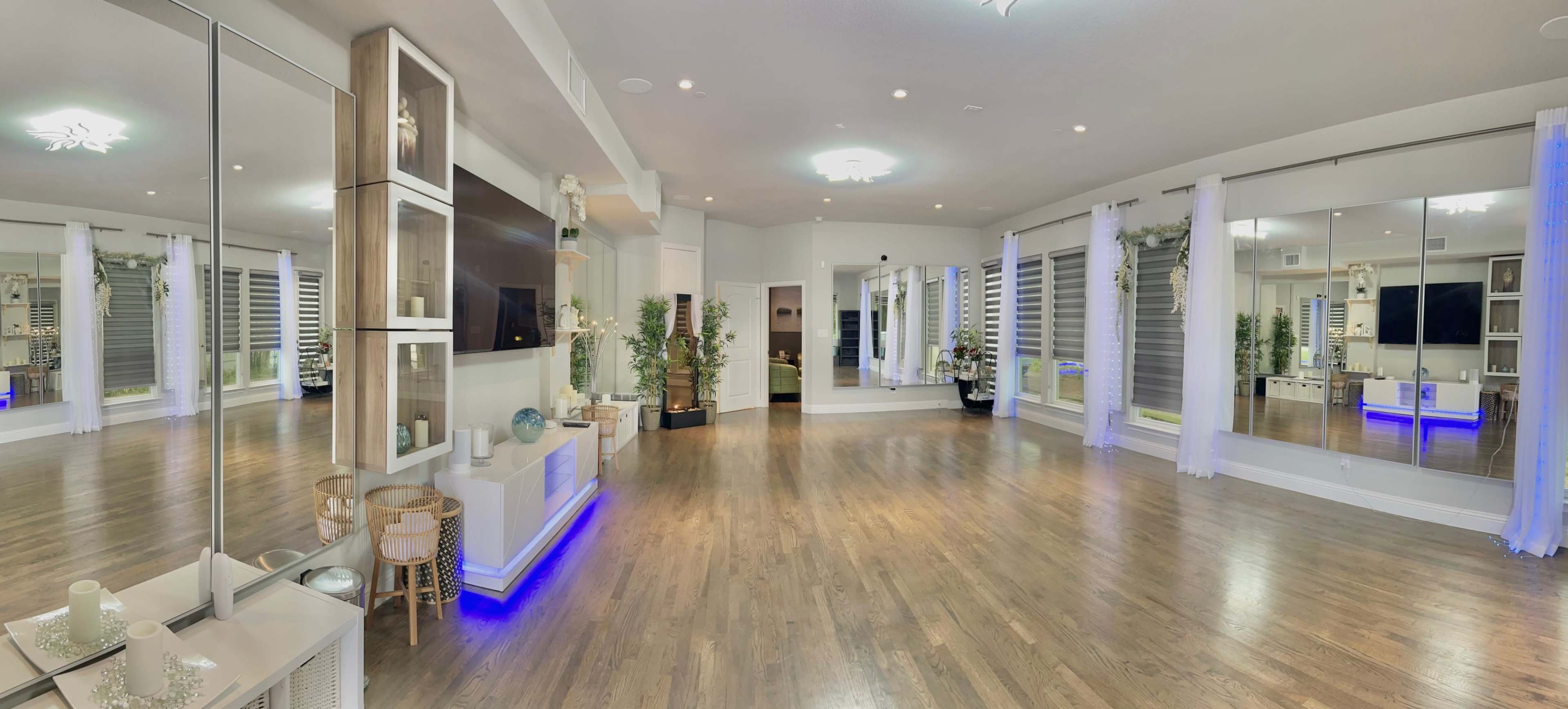 The image shows a spacious, well-lit interior with wooden flooring, multiple mirrors, and minimalist furnishings.