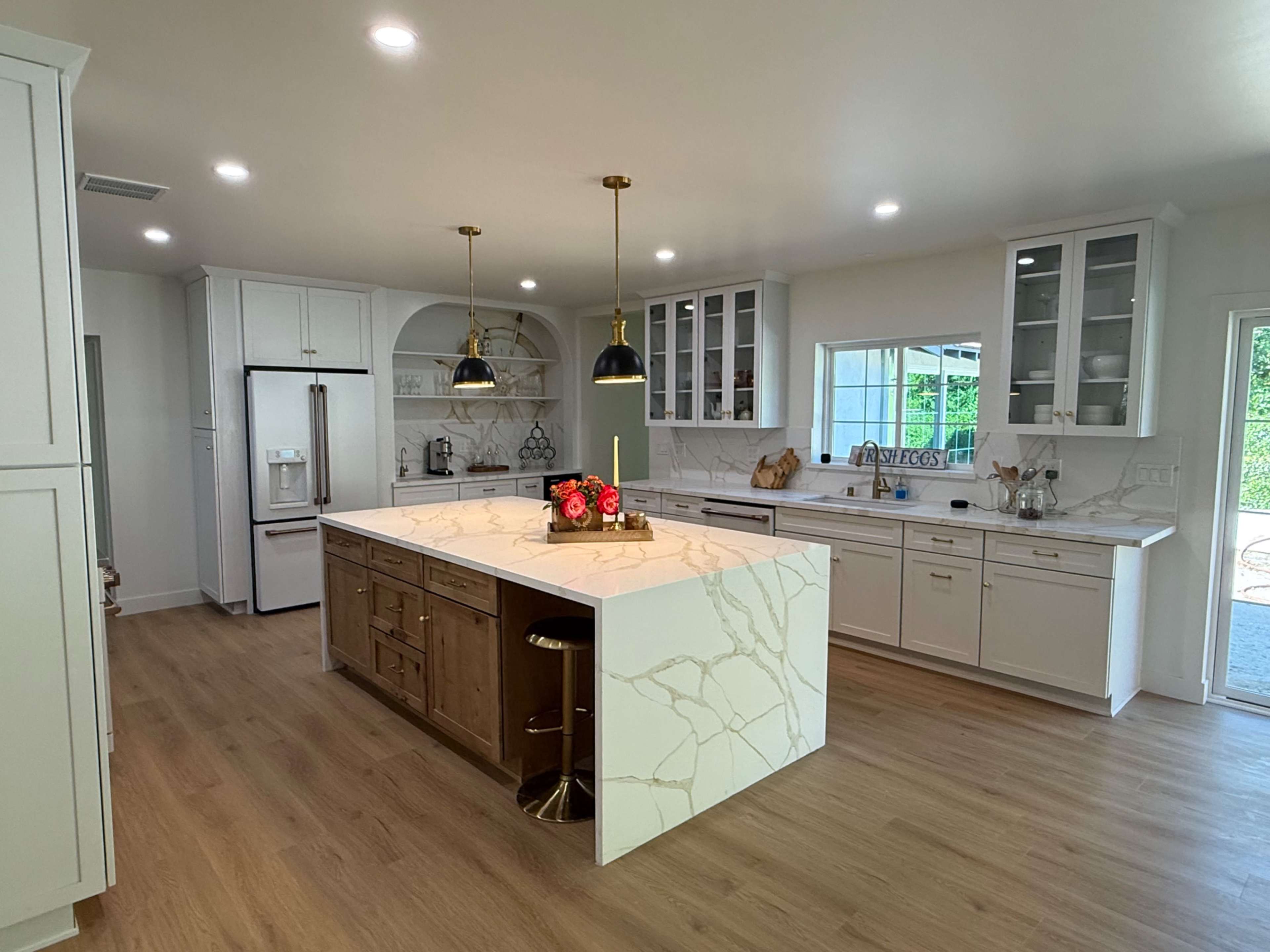 The image shows a modern kitchen with a large island featuring a marble countertop, white cabinetry, and pendant lights.