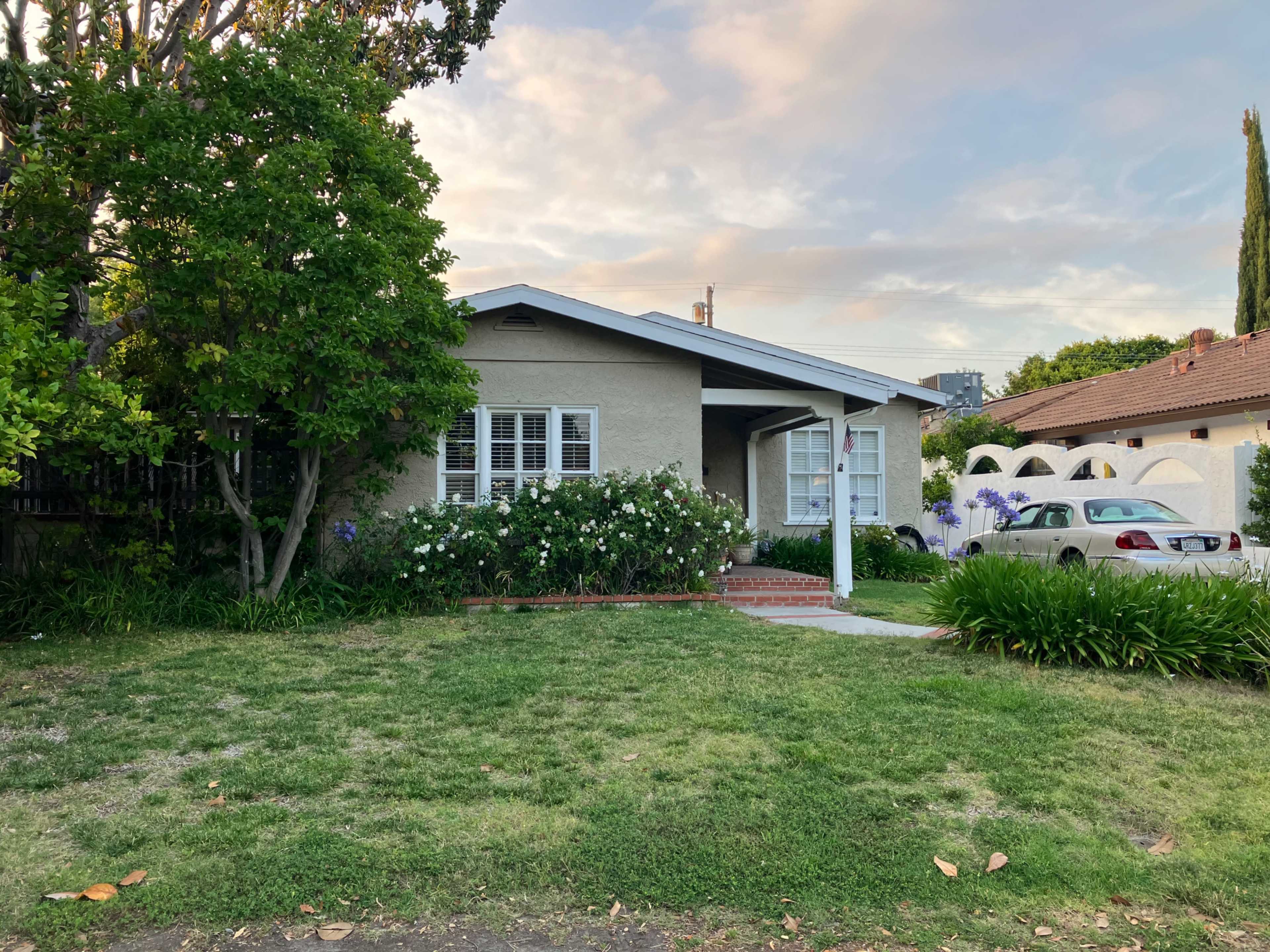 The image shows a single-story house with a landscaped front yard and a parked car in the driveway.